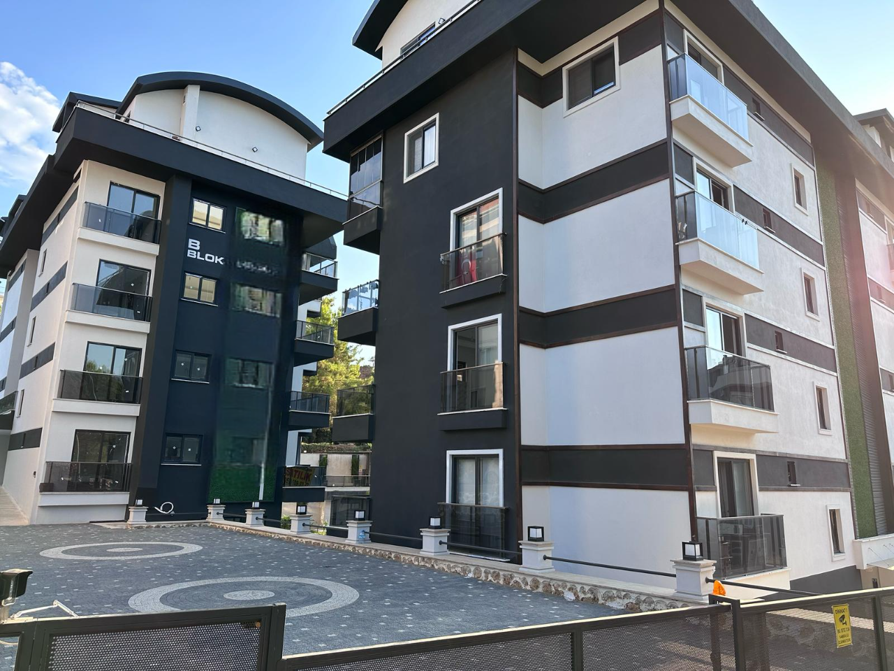 İki konut bloğunun siyah beyaz cepheleri, cam balkonları ve giriş meydanı daireli komplekste