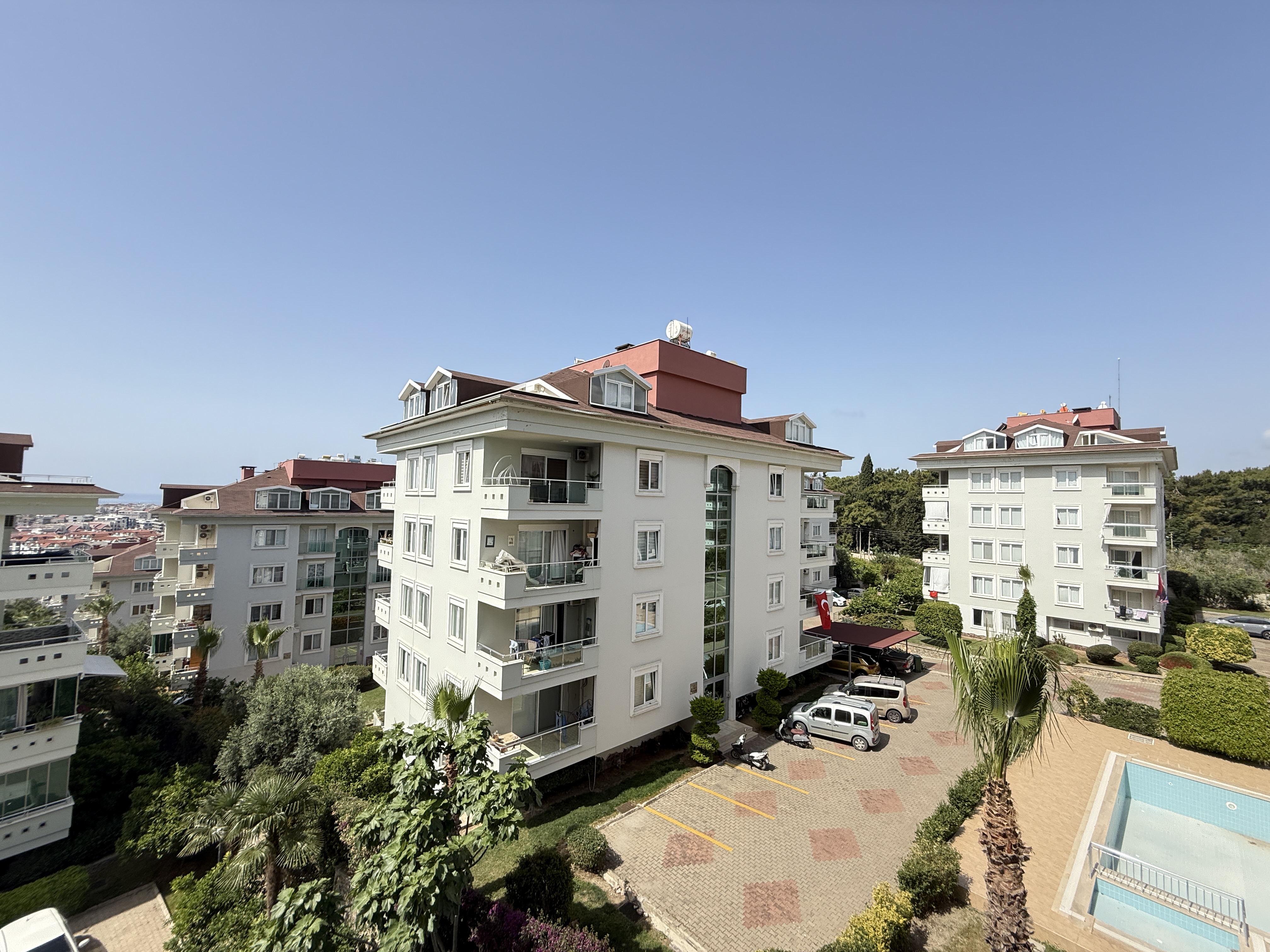 Havuzlu, otoparklı ve palmiyeli iç avlu, kırmızı çatılı konut bloklarının arasında