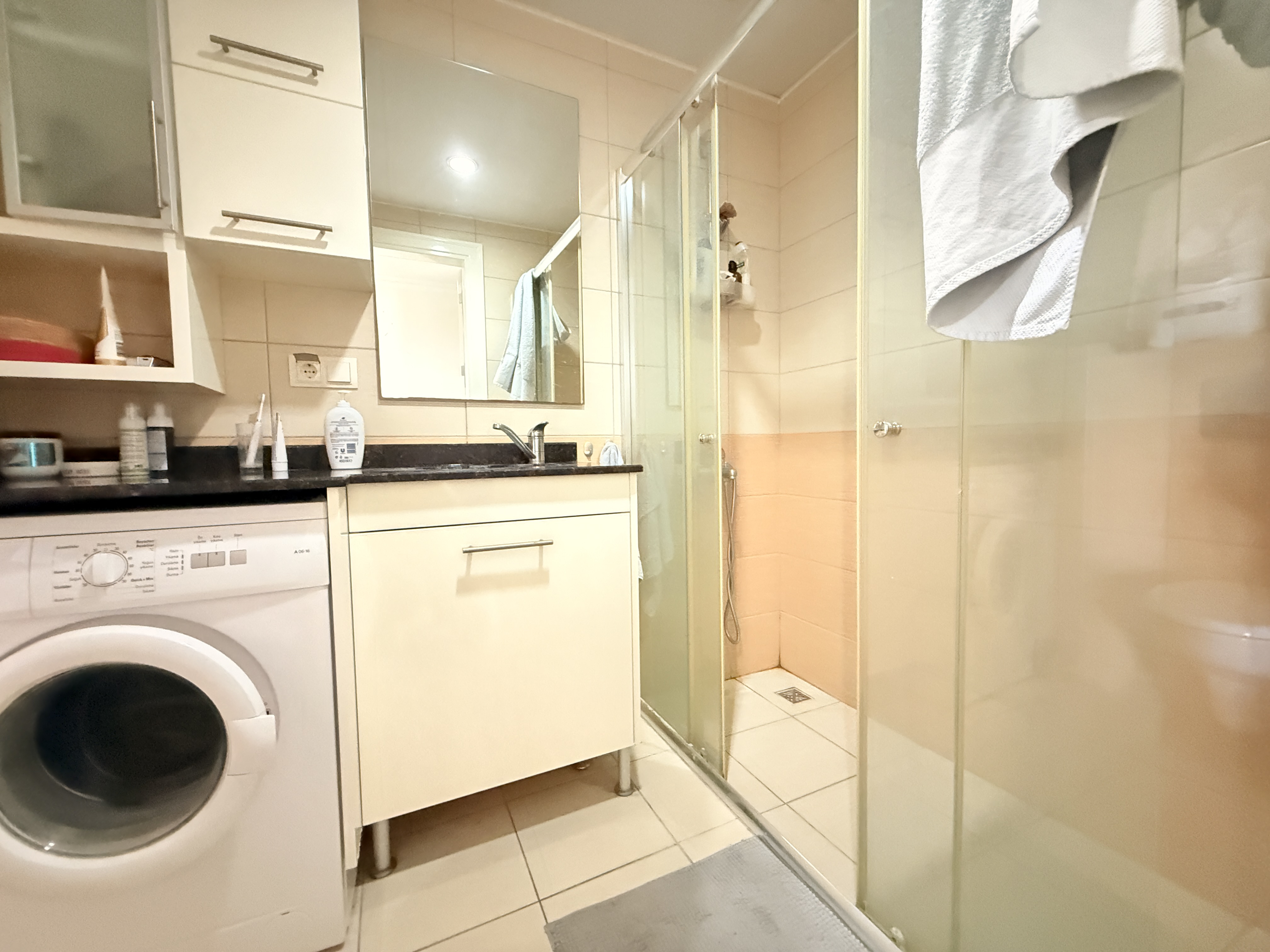 Çamaşır makineli beyaz lavabo dolabı ve cam duş kabini, dairede