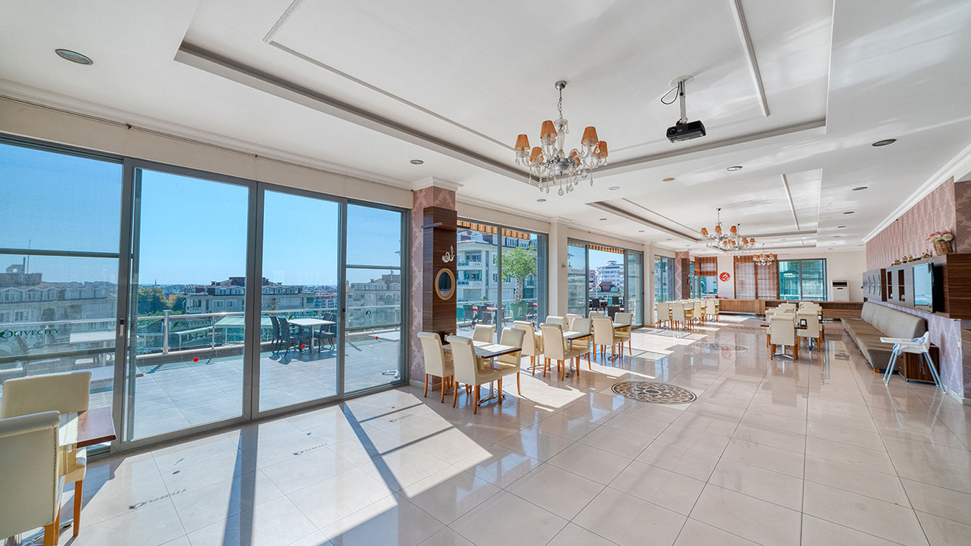 Panoramik camlı restoranda yemek masaları ve deri kanepeler, açık terasa açılır