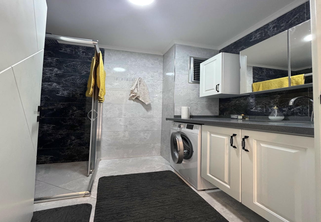 Cam duş kabinli banyo Kestel'deki dairede çamaşır makinesi ve siyah gri fayanslarla