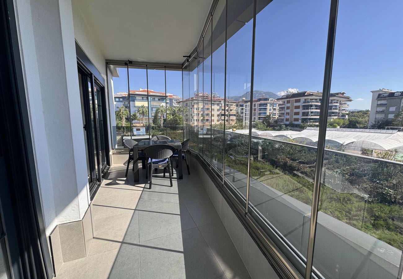 Panoramik camlı kapalı teras yemek masası ve uzaktaki dağ yamacına bakan yeşil alanla