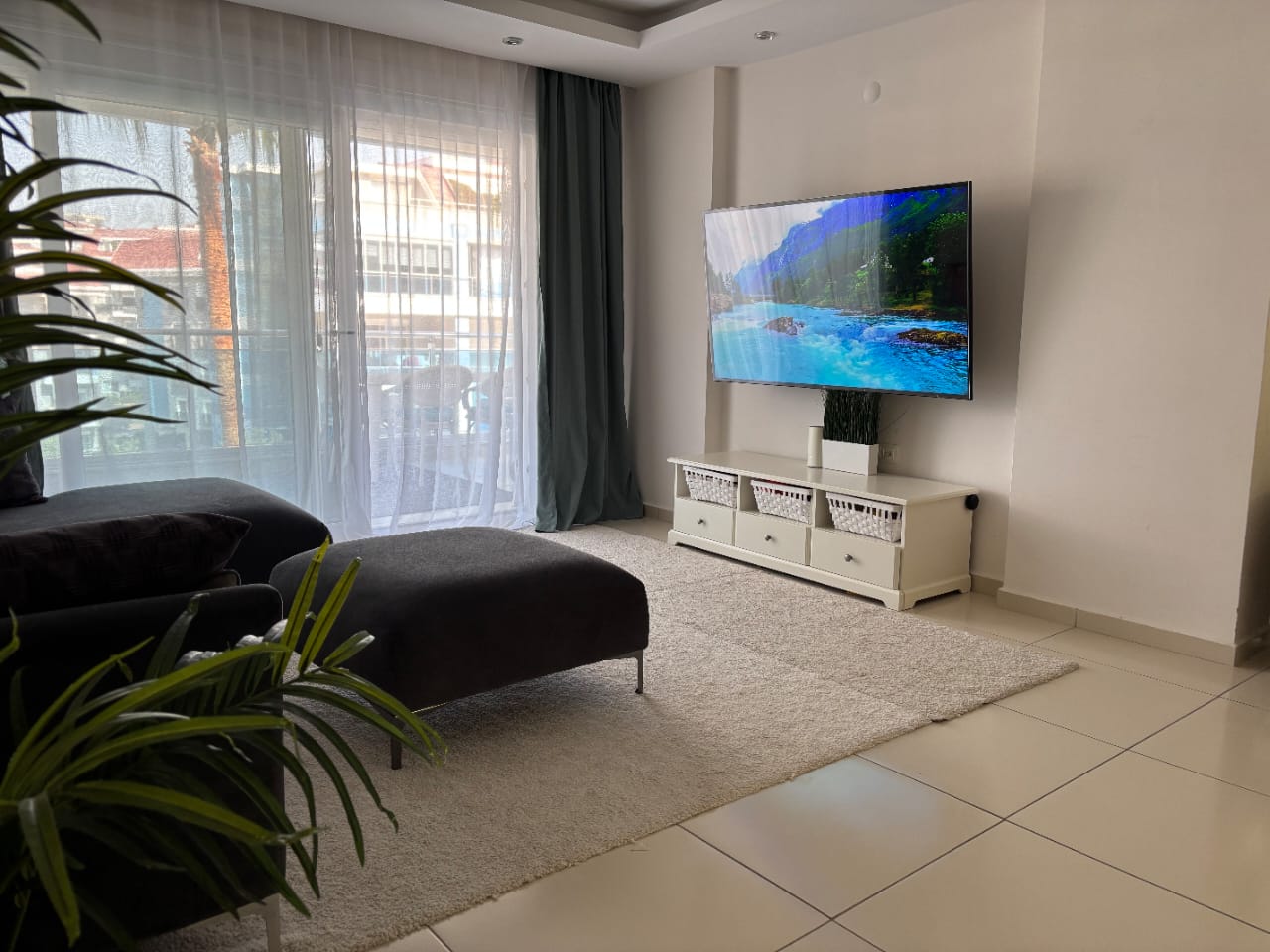 Televizyonlu salonda koyu gri köşe koltuk ve panoramik pencere, konut içinde