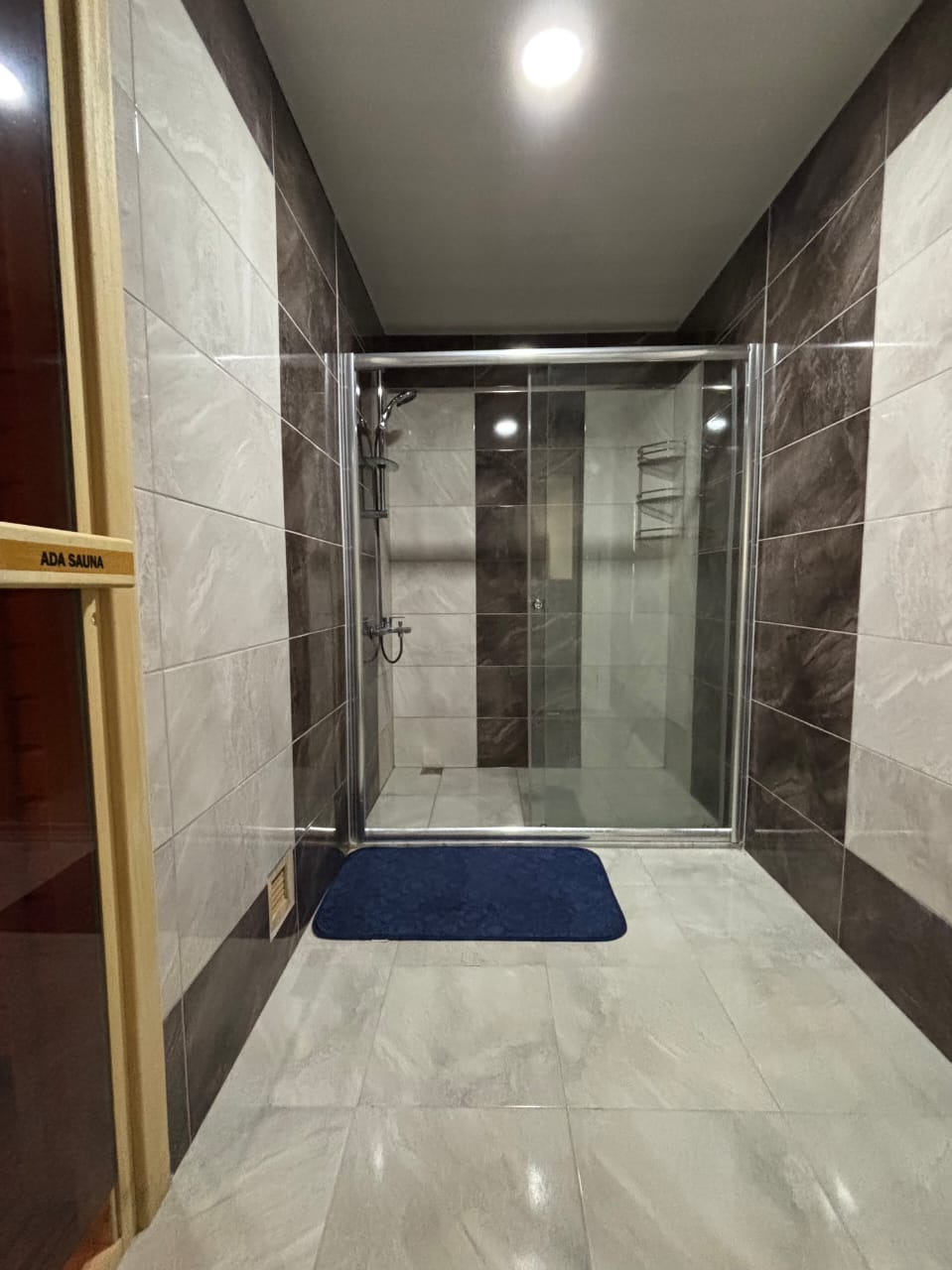 Cam duş kabinli banyoda gri kahverengi fayans ve sauna kapısı, Kestel’deki dairede