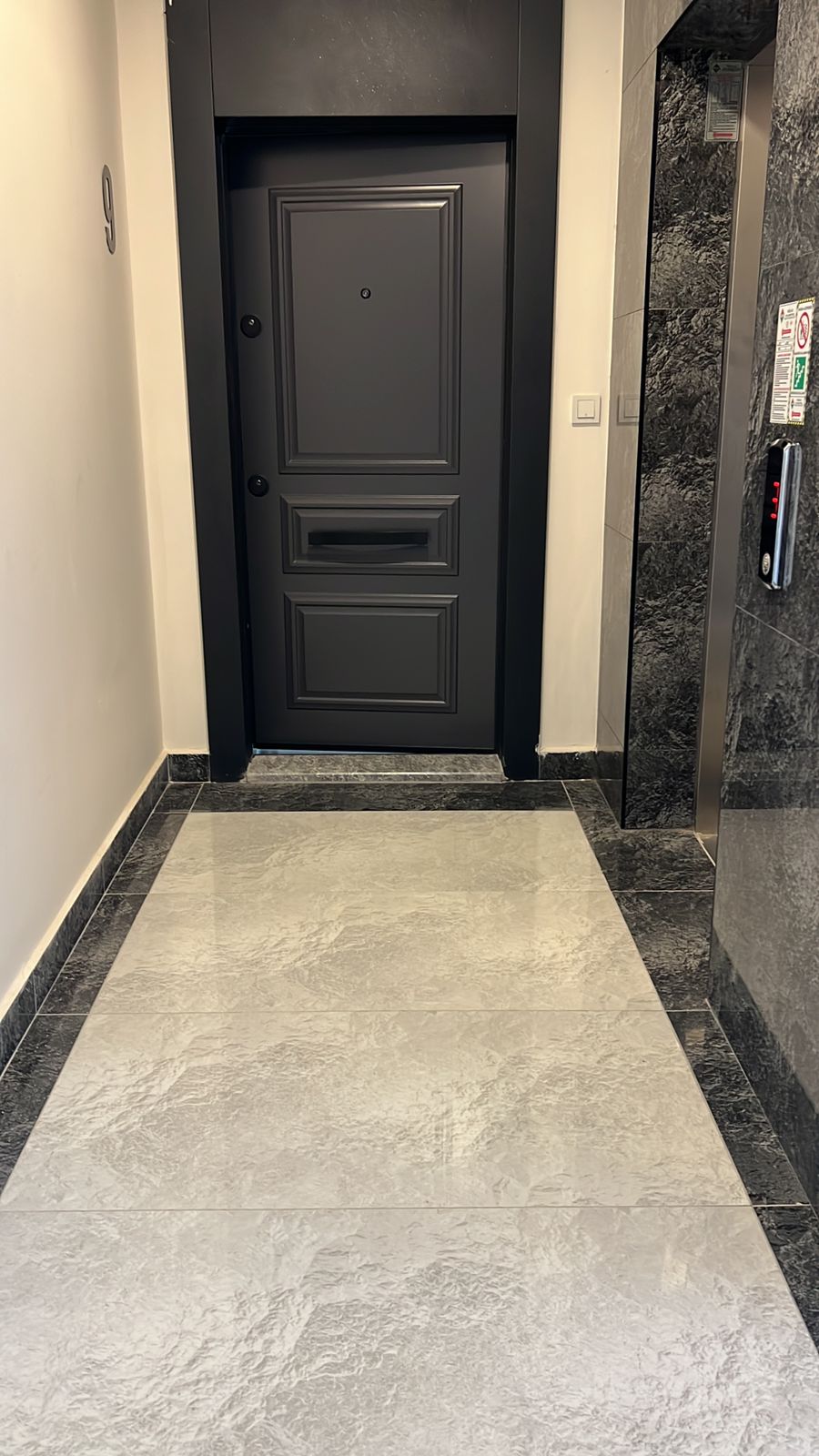 Siyah giriş kapısı ve mermer kaplamalı duvar Oba’daki penthouse koridorunda görülüyor