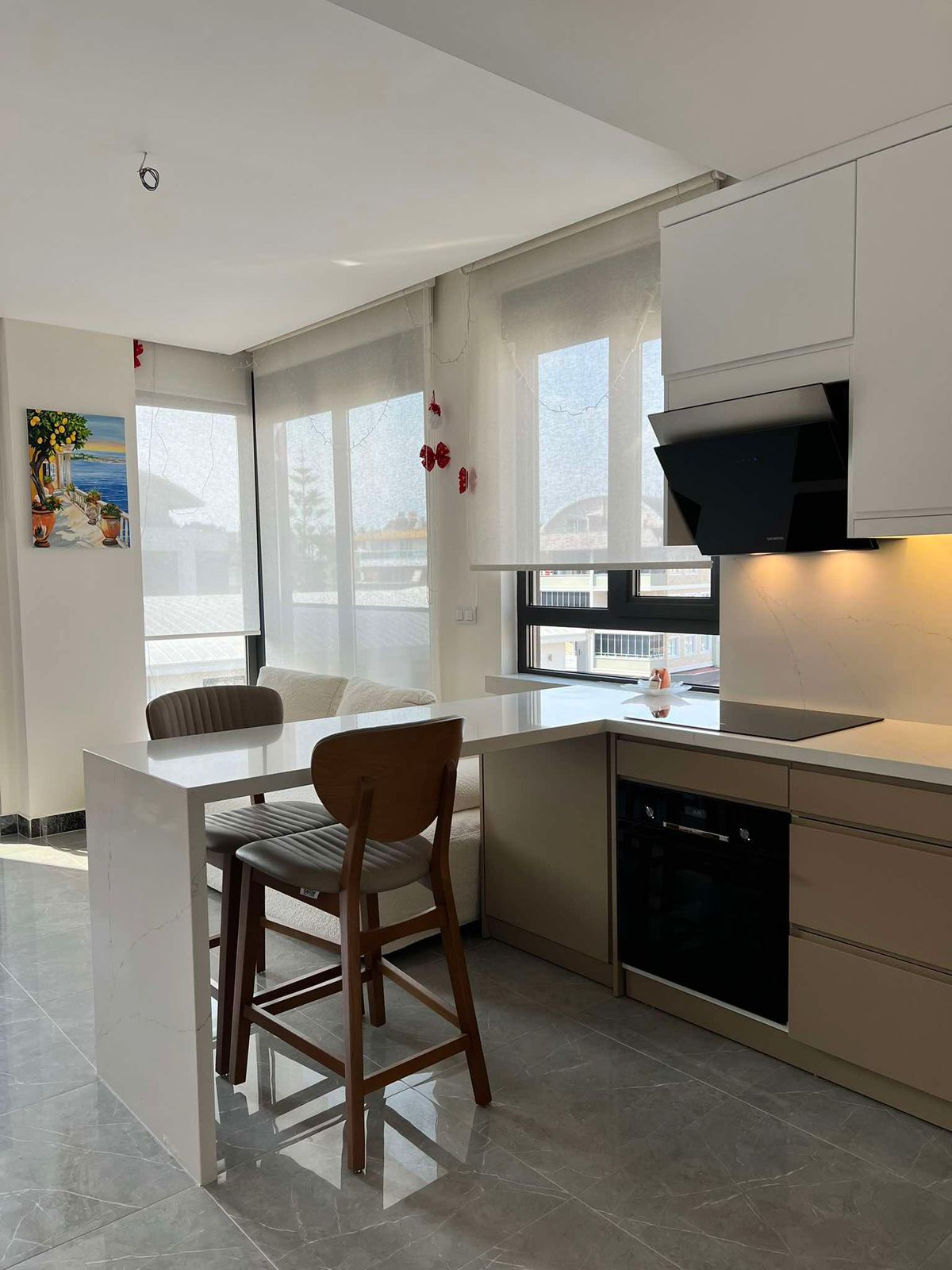 Beyaz dolaplı, yarımadalı ve siyah davlumbazlı mutfak Oba’daki penthouse içinde yer alıyor