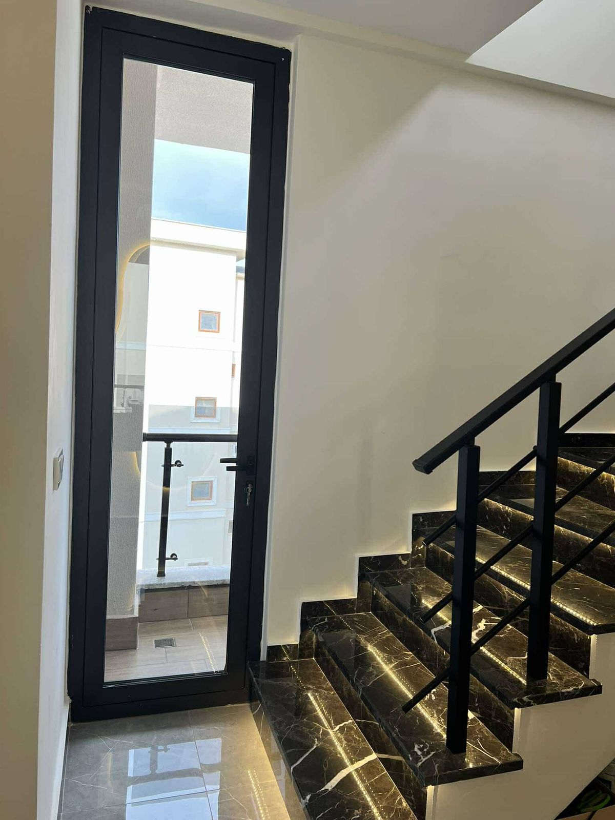 Koyu mermer basamaklı merdiven ve panoramik siyah çerçeveli kapı Oba’daki penthouse’ta yer alıyor