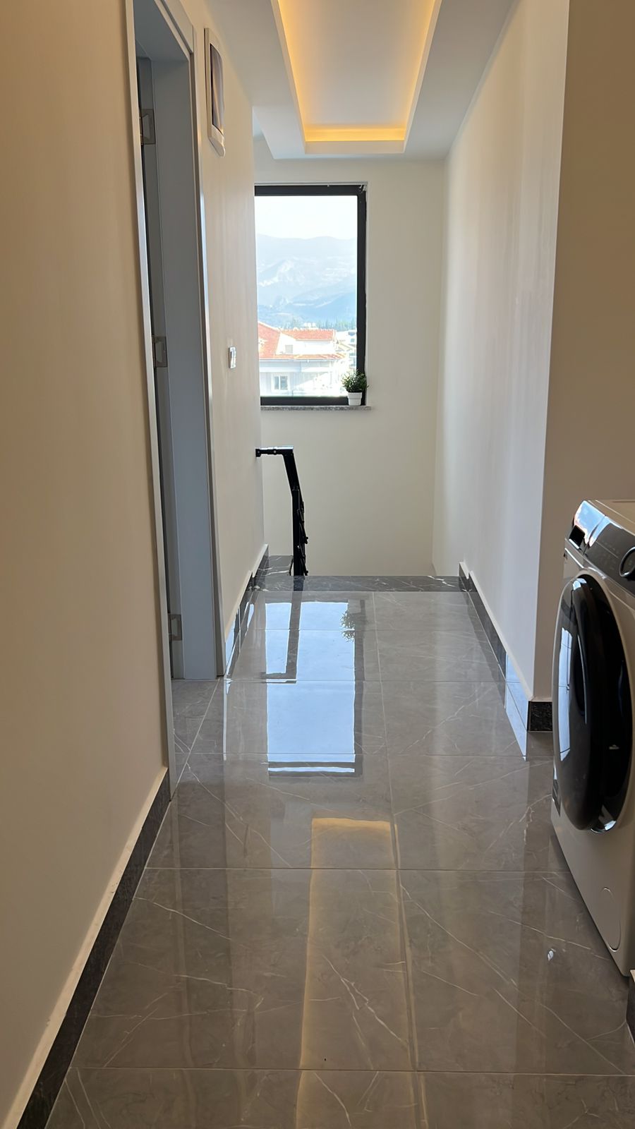 Çamaşır makineli dar koridor ve uçtaki panoramik pencere penthouse’un içinde yer alıyor
