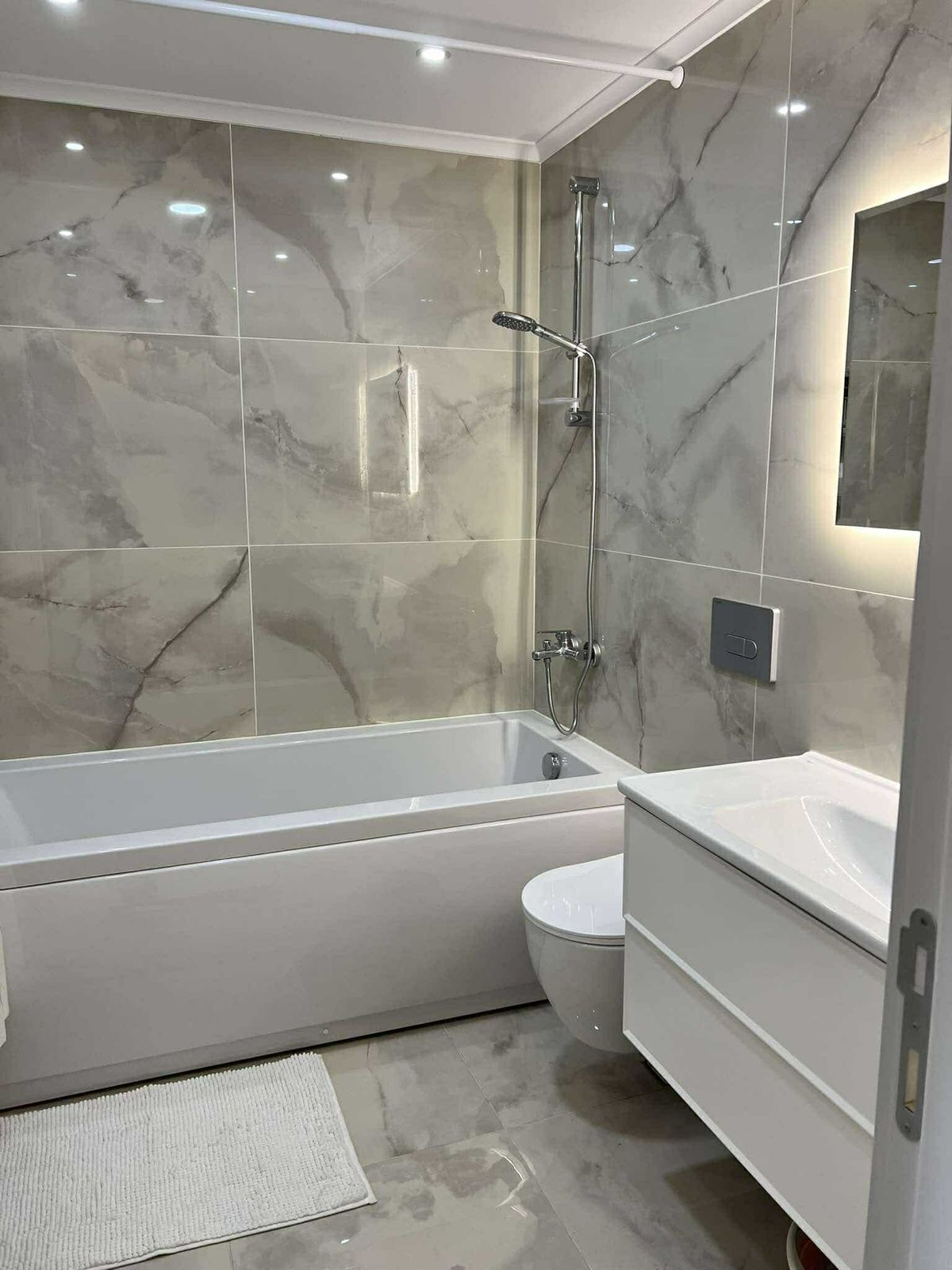 Beyaz küvetli ve ışıklı aynalı banyo Oba’daki konutta mermer kaplamalarla tamamlanıyor