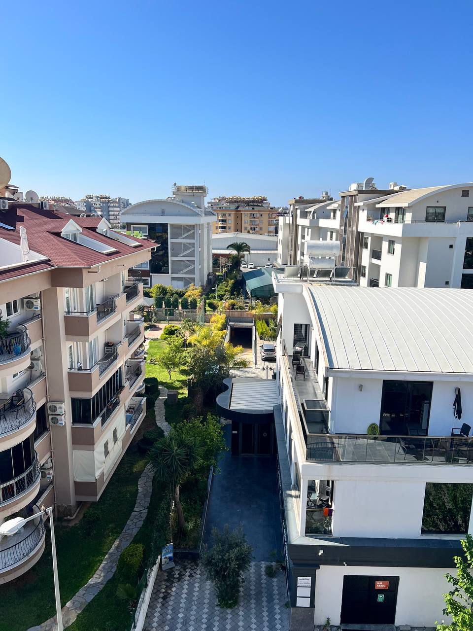 Palmiyeli bahçe yolu ve beyaz konut blokları Oba’daki 2+1 rezidans kompleksinin arazisinde bulunuyor
