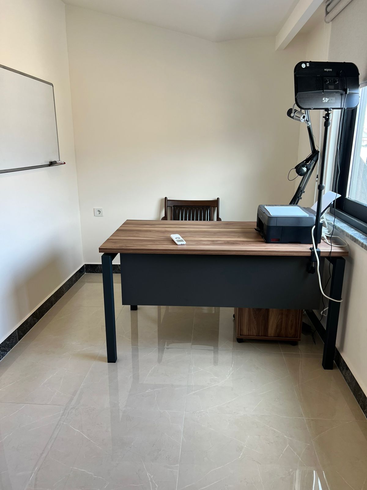 Ahşap masalı çalışma odasında tripodlu projektör ve beyaz pano pencerenin yanında yer alıyor