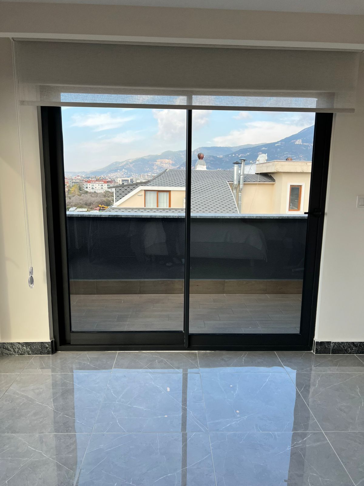 Panoramik balkon kapısı ve dağlık yerleşim manzarası, satılık penthouse’un terasından görülüyor