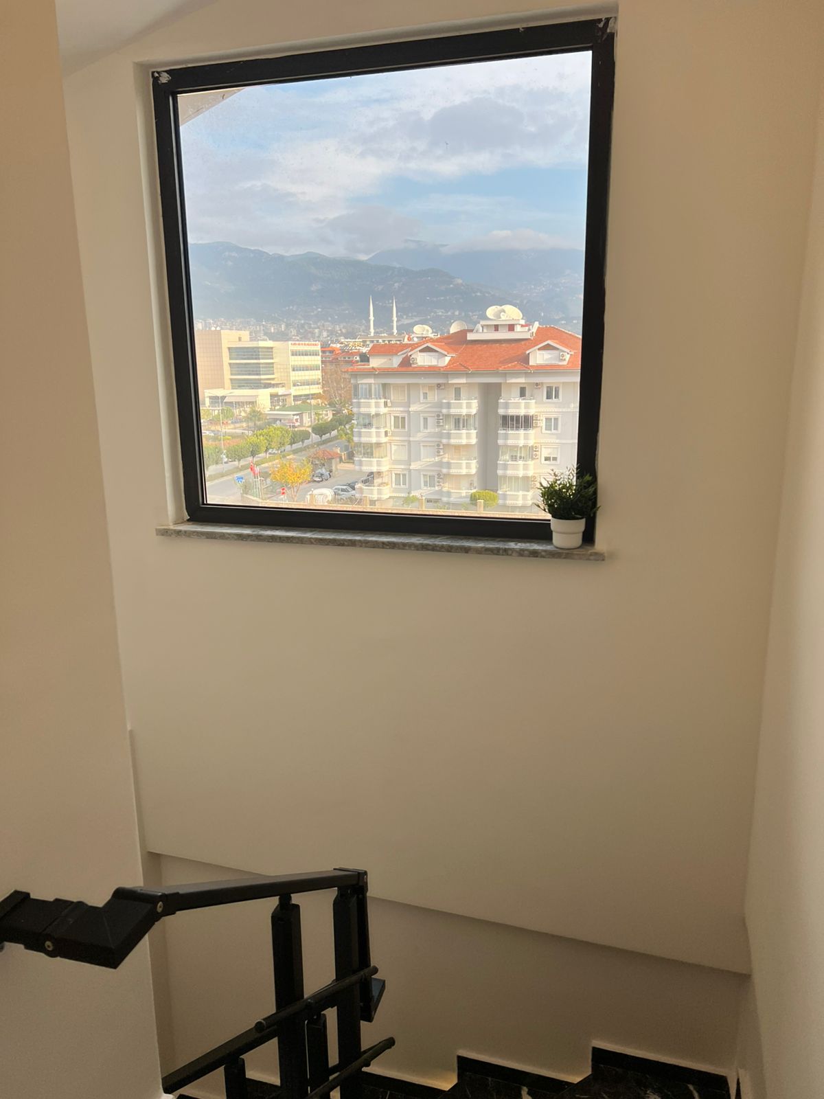Panoramik pencereli merdiven sahanlığı, penthouse’un şehir ve dağ manzarasını gösteriyor