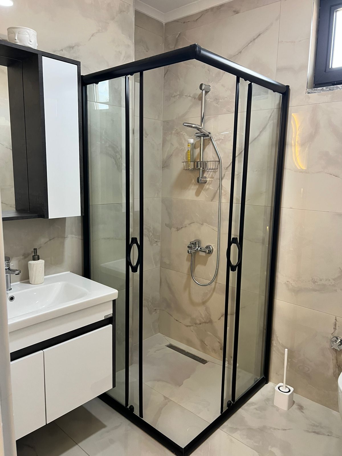 Siyah profilli cam duş kabinli banyo Oba’daki penthouse’un mermer duvarlarını gösteriyor