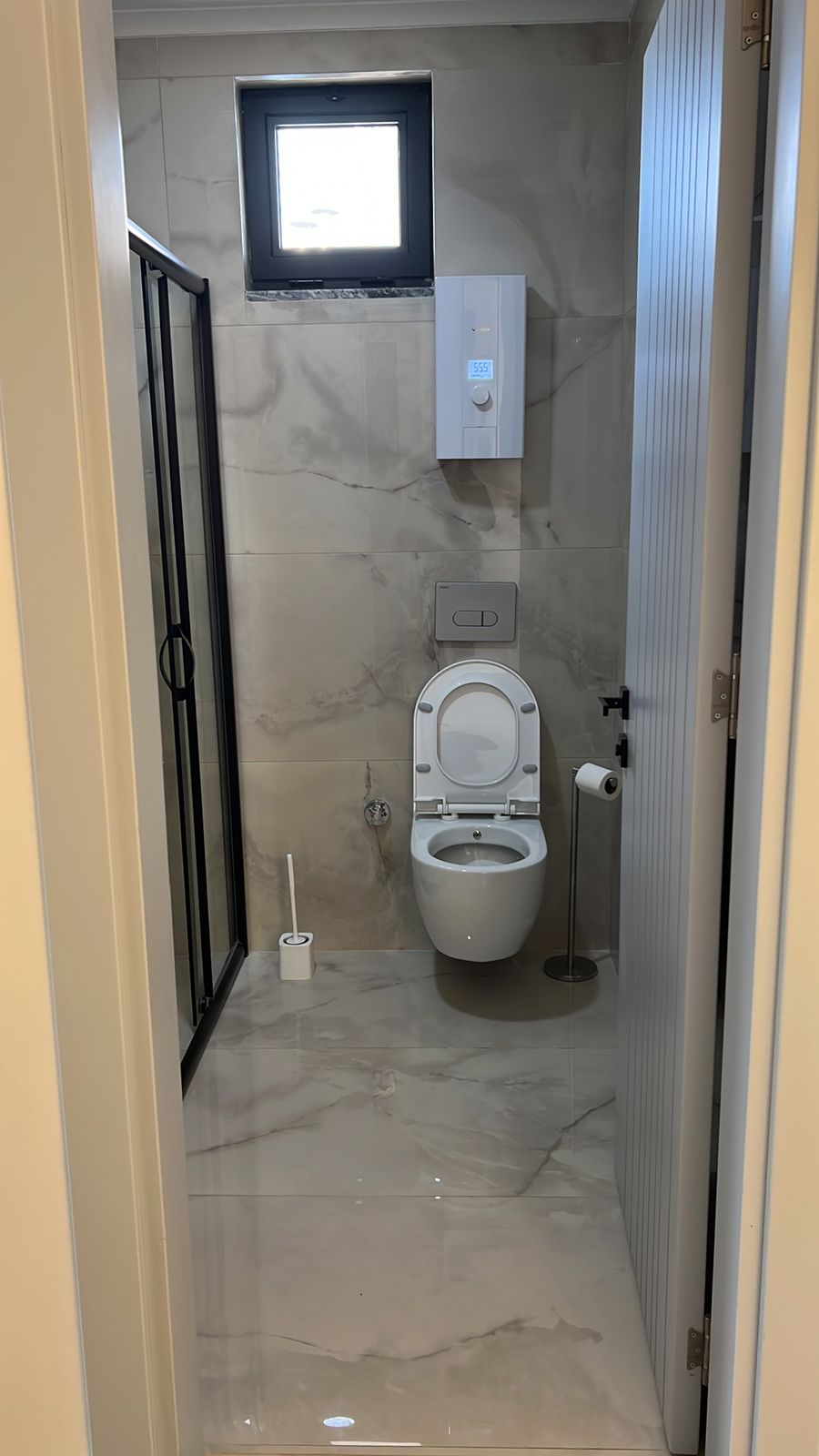 Asma klozetli ve küçük pencereli banyo çatı katı dairenin mermer kaplamalarıyla görülüyor