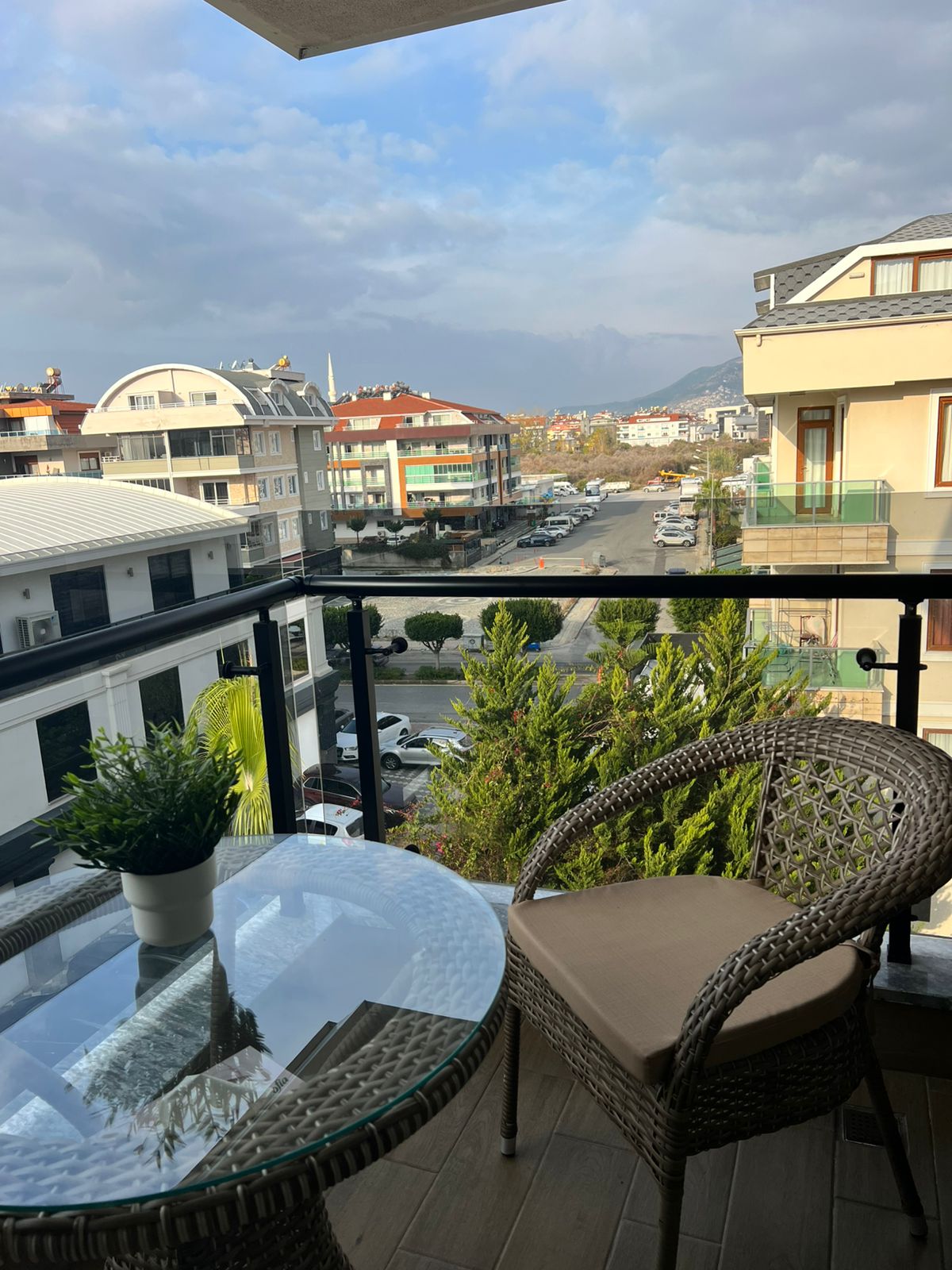 Yuvarlak cam masa ve minderli hasır koltuk, satılık penthouse balkonunda dağ sırtına bakıyor