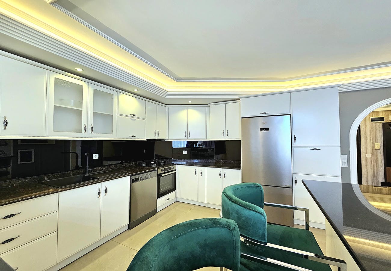 Beyaz dolaplı mutfak penthouse dairesinde siyah parlak panel ve yeşil sandalyelerle