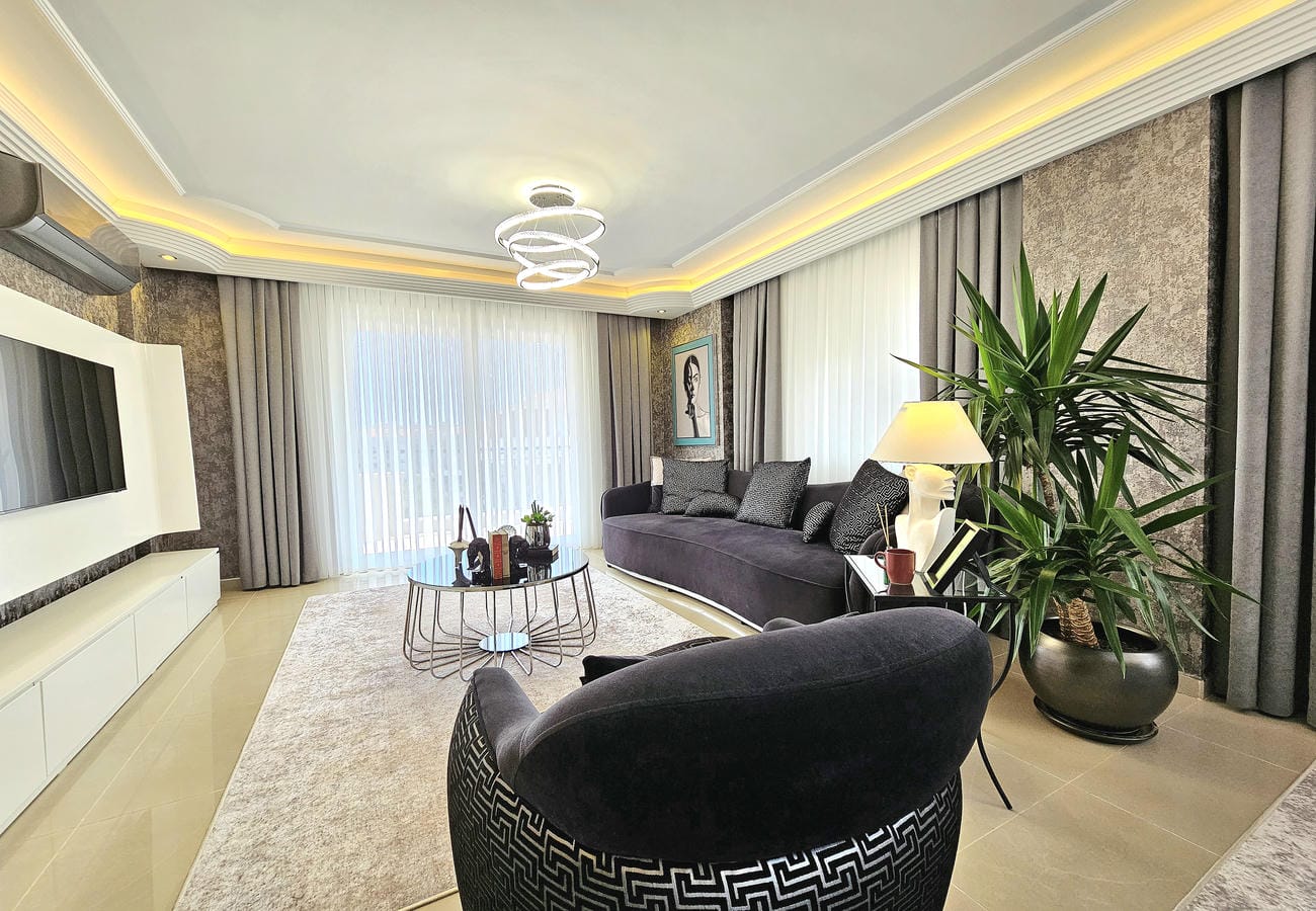 Televizyonlu salon Oba’da satılık çatı katı dairede siyah koltuk ve açık halıyla