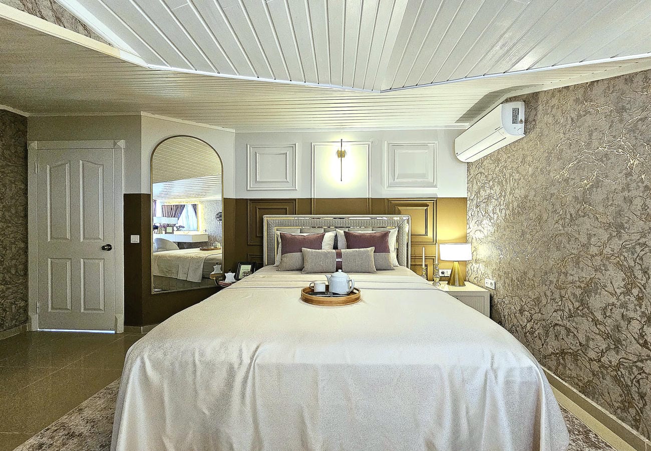 Beyaz yataklı yatak odası penthouse dairesinde mermer desenli duvar ve kemerli aynayla