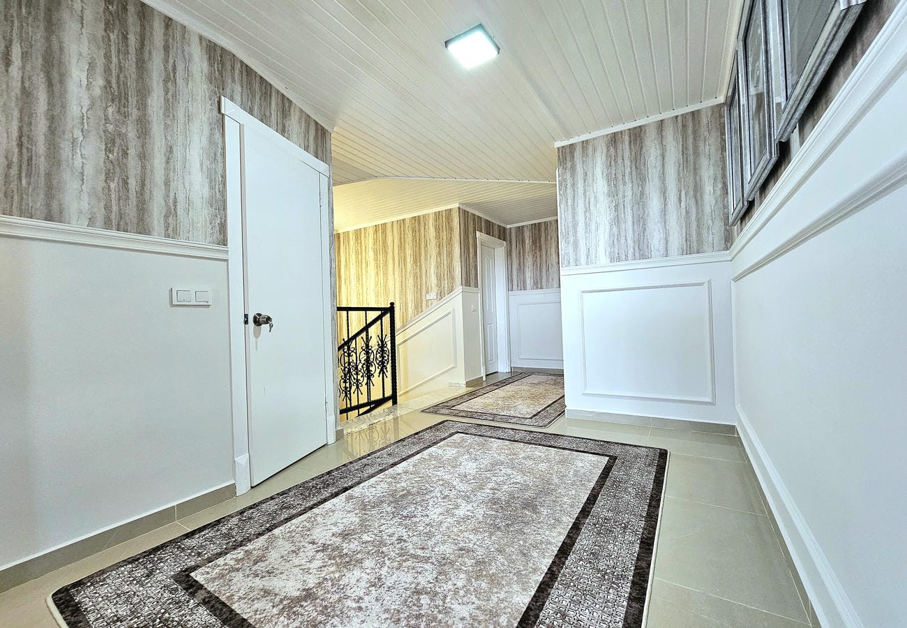 Uzun koridor penthouse dairesinde geometrik kenarlı halılar ve siyah merdiven korkuluğuyla