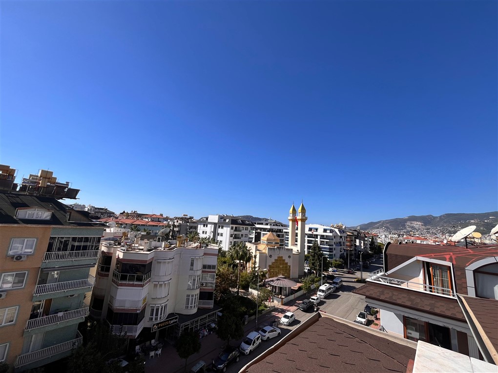Dağ yamacına ve çift minareli camiye bakan şehir manzarası satılık penthouse’dan