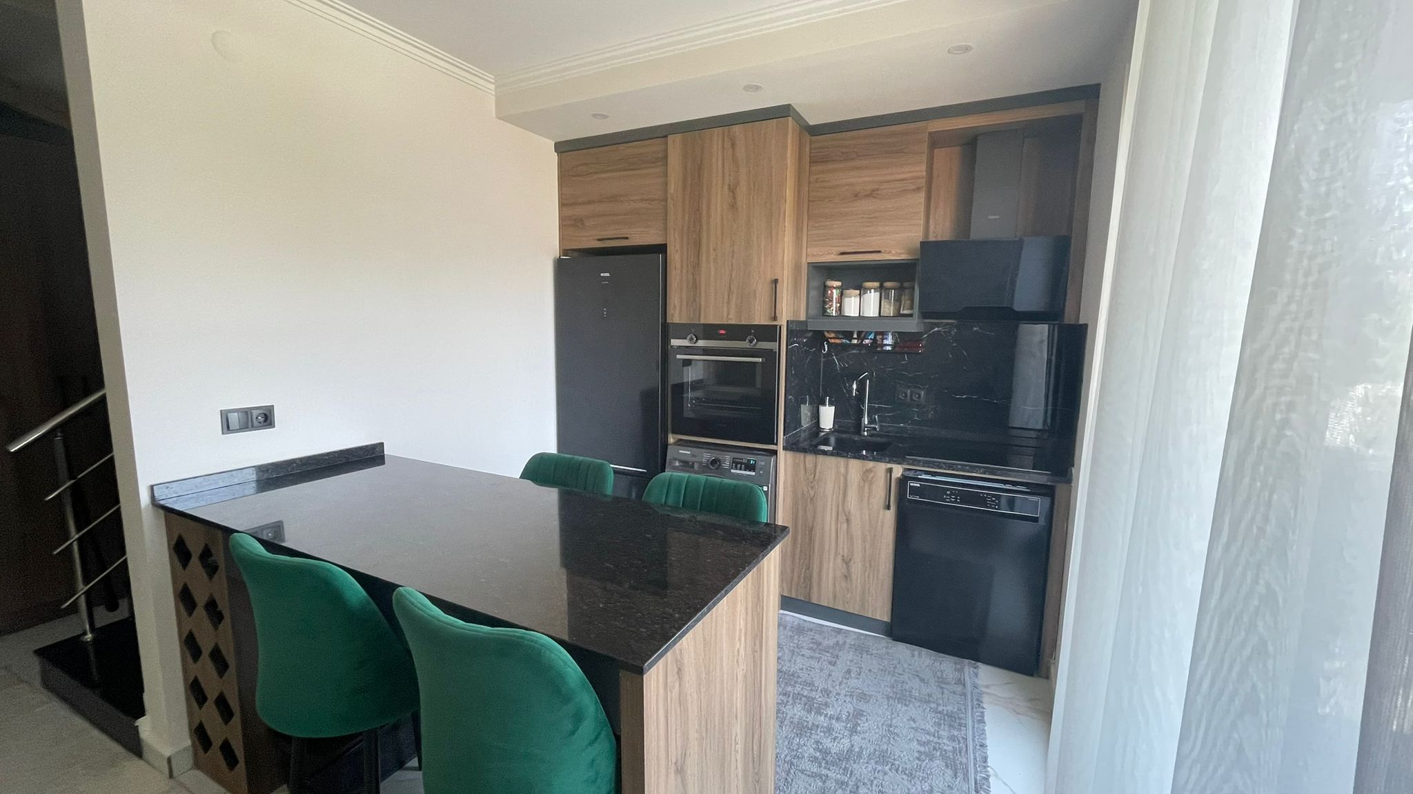 Mutfakta siyah tezgâhlı ada, ahşap dolaplar ve siyah buzdolabı Oba'daki penthouse içinde