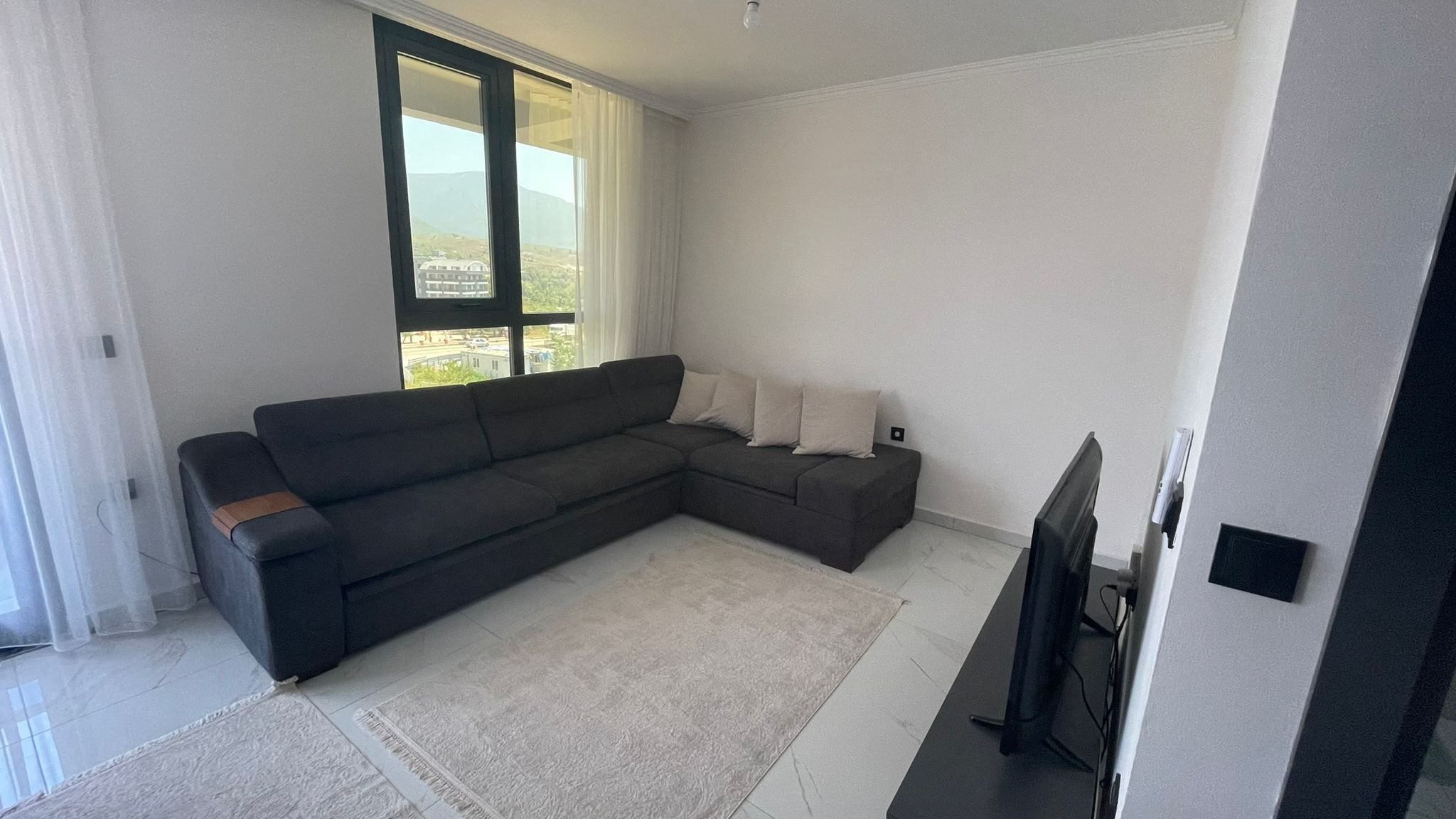 Oturma odasında koyu gri köşe kanepe ve dağ manzaralı panoramik pencere Türkiye'de satılık penthouse içinde