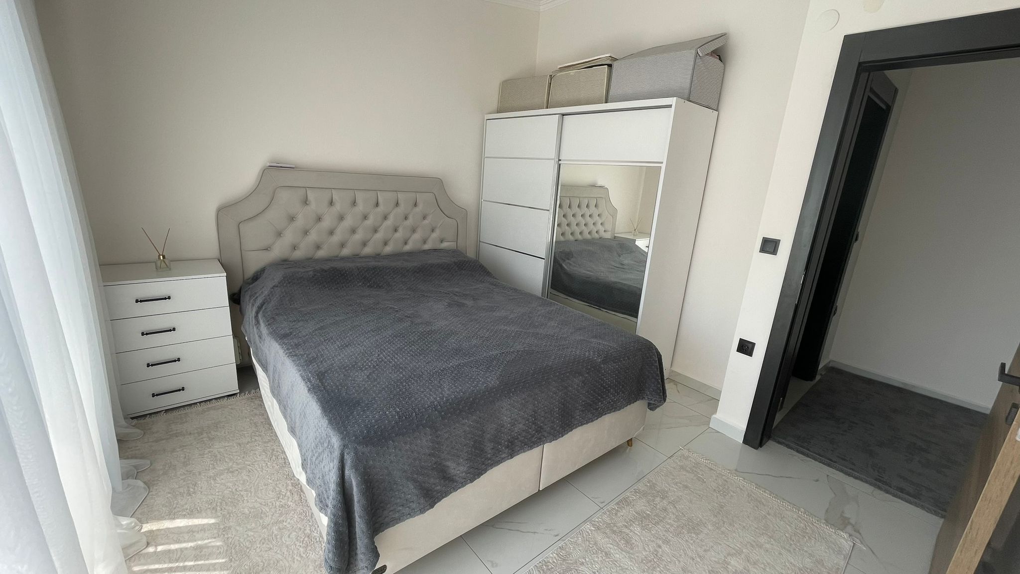 Yatak odasında aynalı beyaz dolap, çift kişilik yatak ve panoramik pencere Oba'daki penthouse içinde