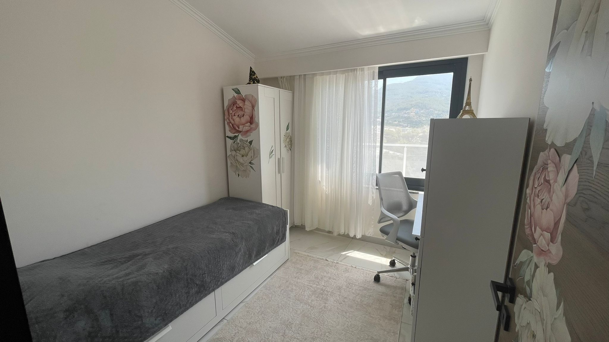 Yatak odasında tek kişilik yatak, çalışma masası ve pencereden görünen dağlar penthouse içinde