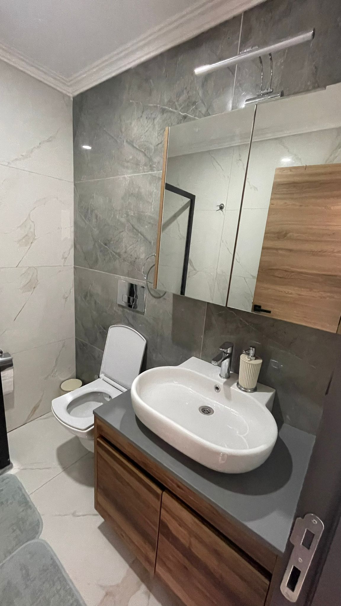 Banyoda oval lavabo, ahşap dolap ve büyük duvar aynası