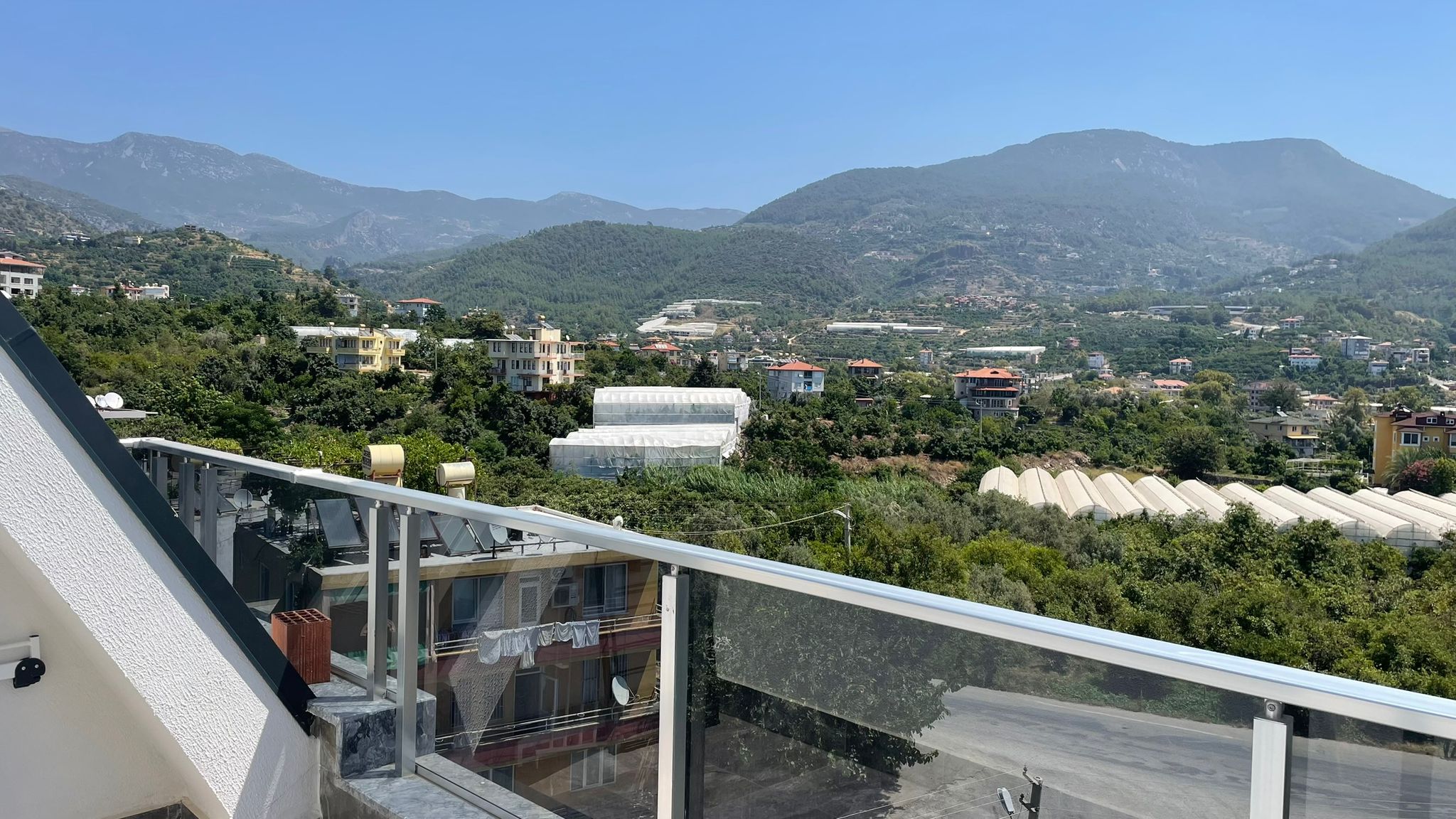 Terastan dağlar, seralar ve yamaç evleri görünürken satılık penthouse manzarası