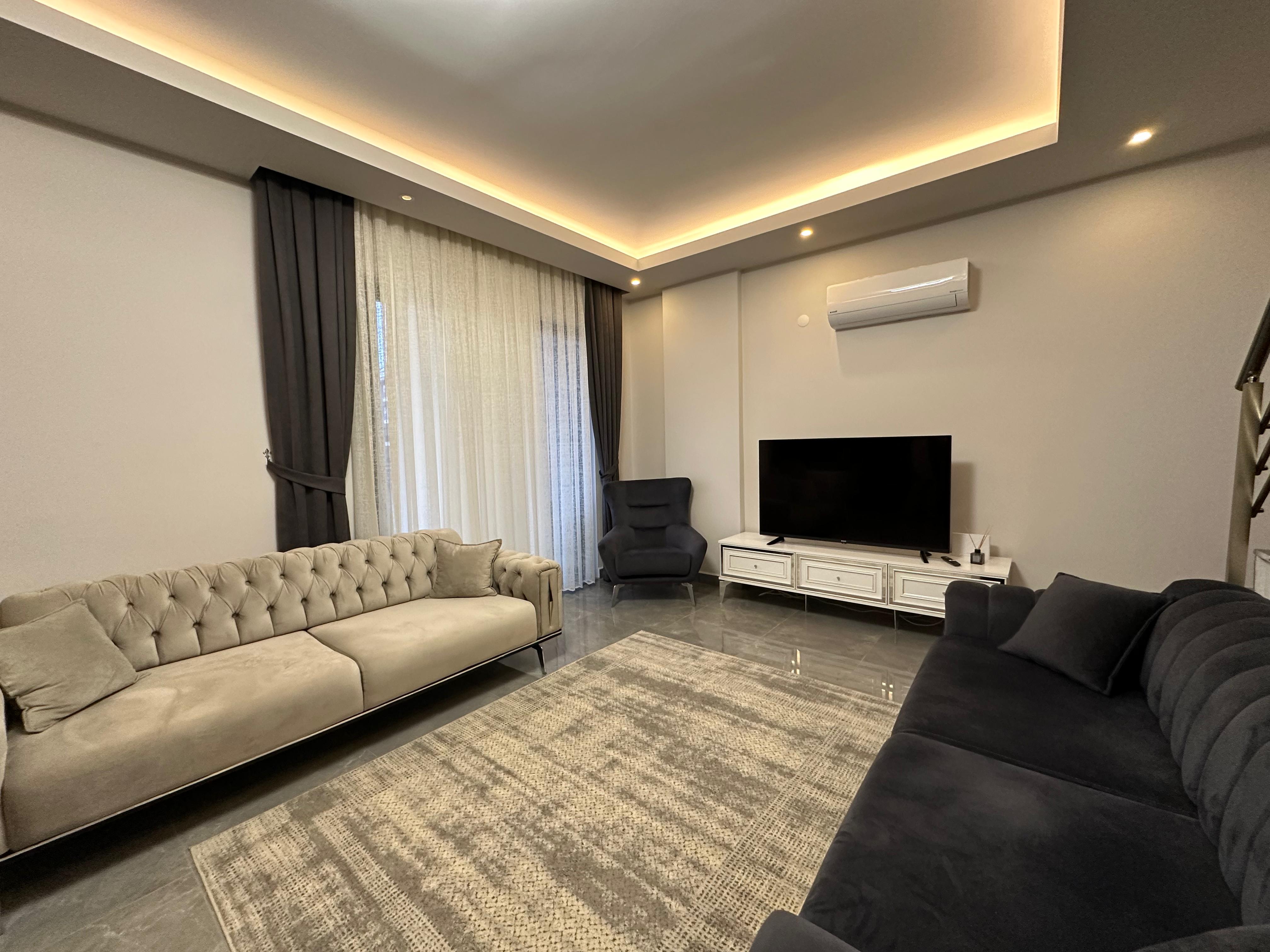 Living room with two sofas, a TV and panoramic window in a penthouse in Oba