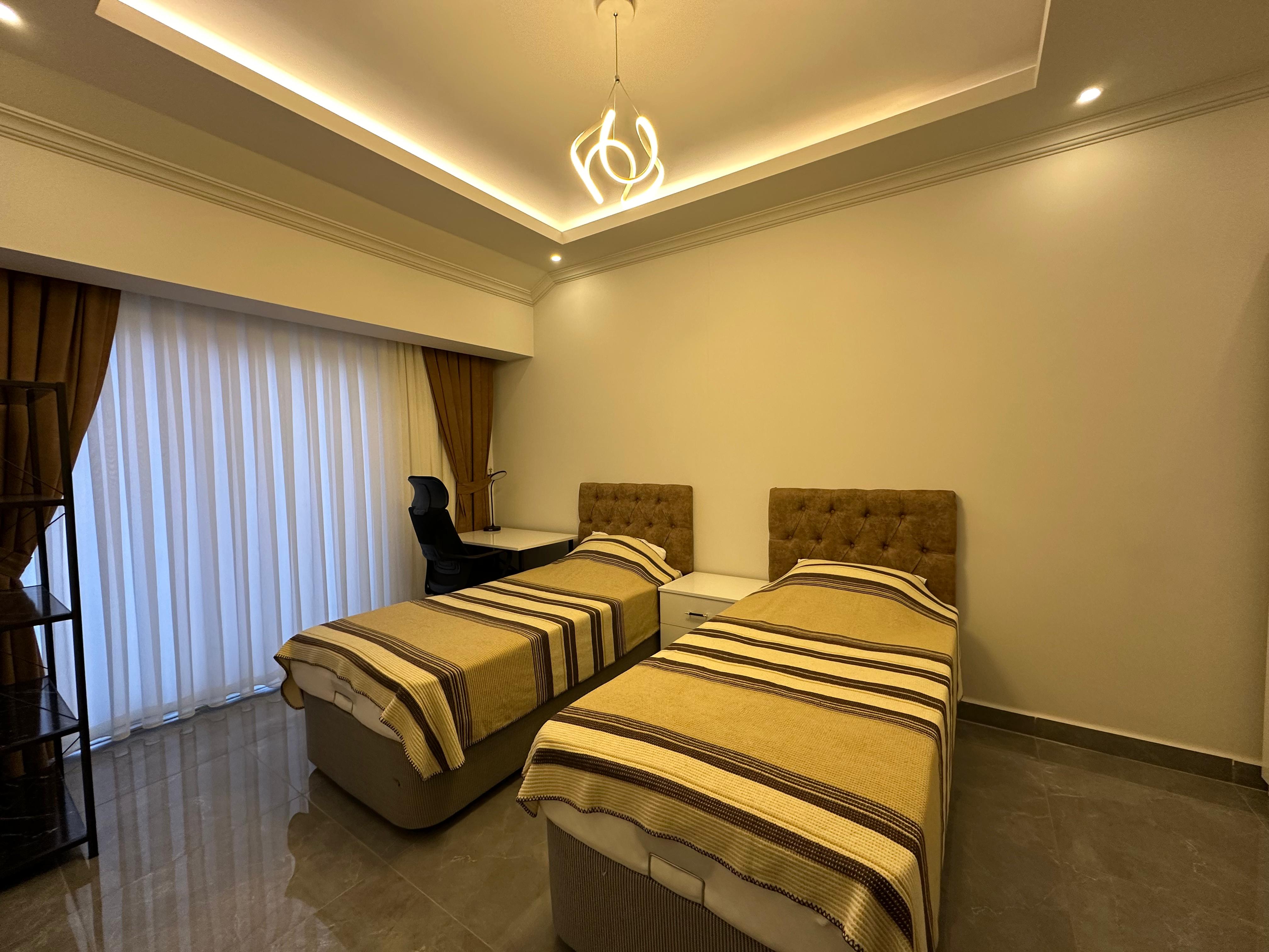 Twin bedroom with a desk, panoramic window and upholstered headboards in a residence in Oba