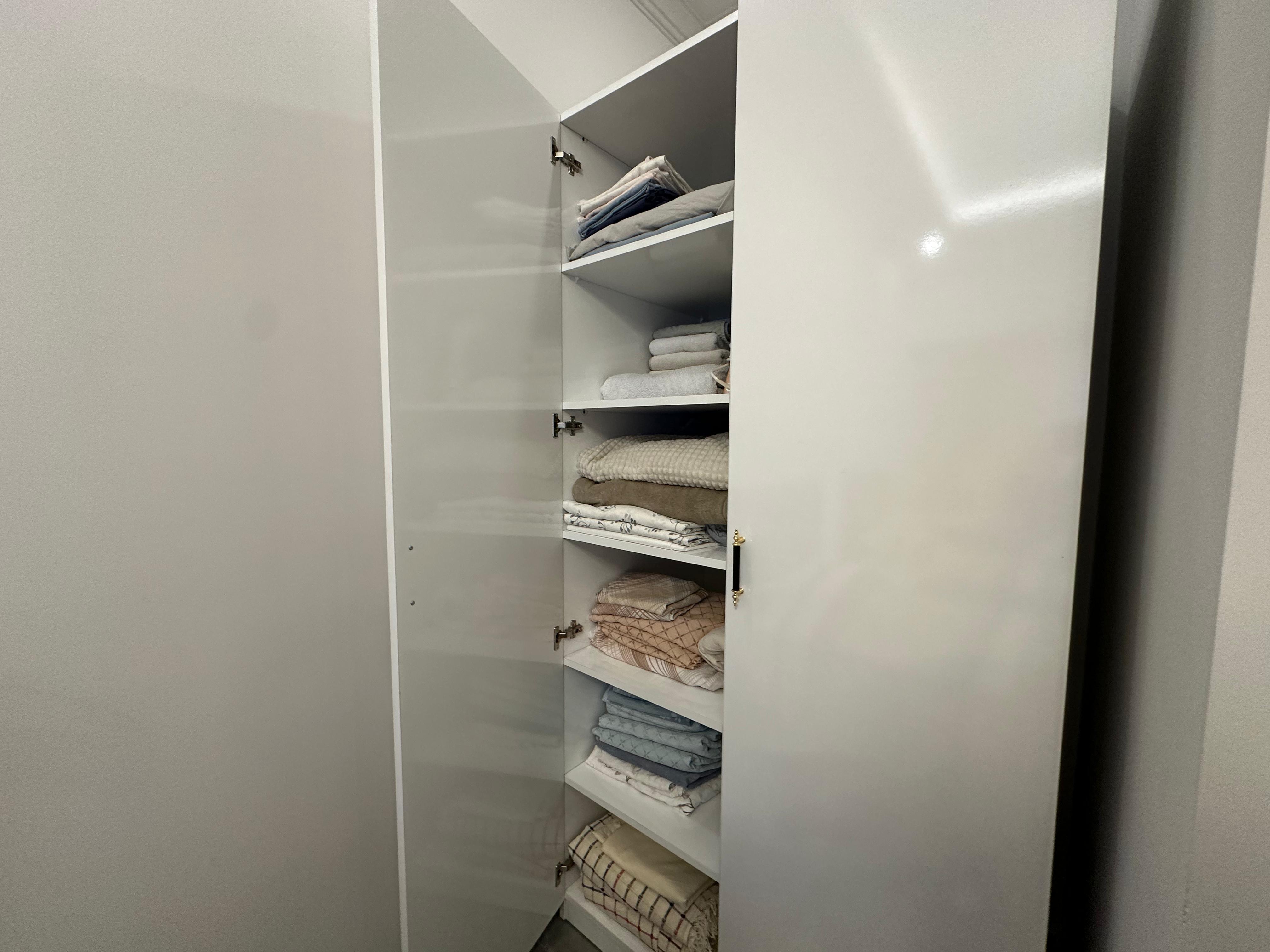 Walk-in wardrobe with an open white cabinet, folded towels and narrow storage space