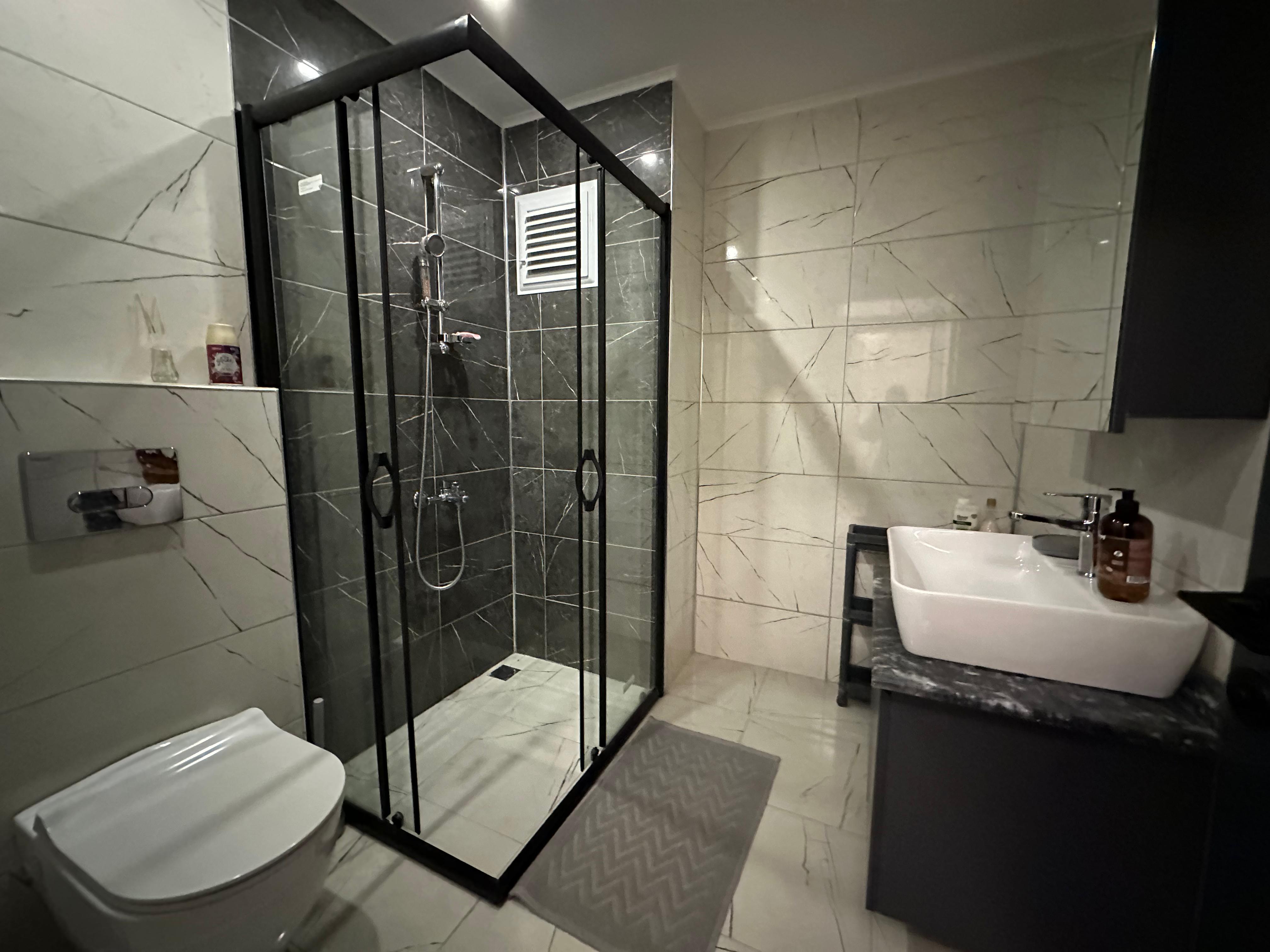 Bathroom with a glass shower enclosure, black fittings and marble tiles in a penthouse in Oba