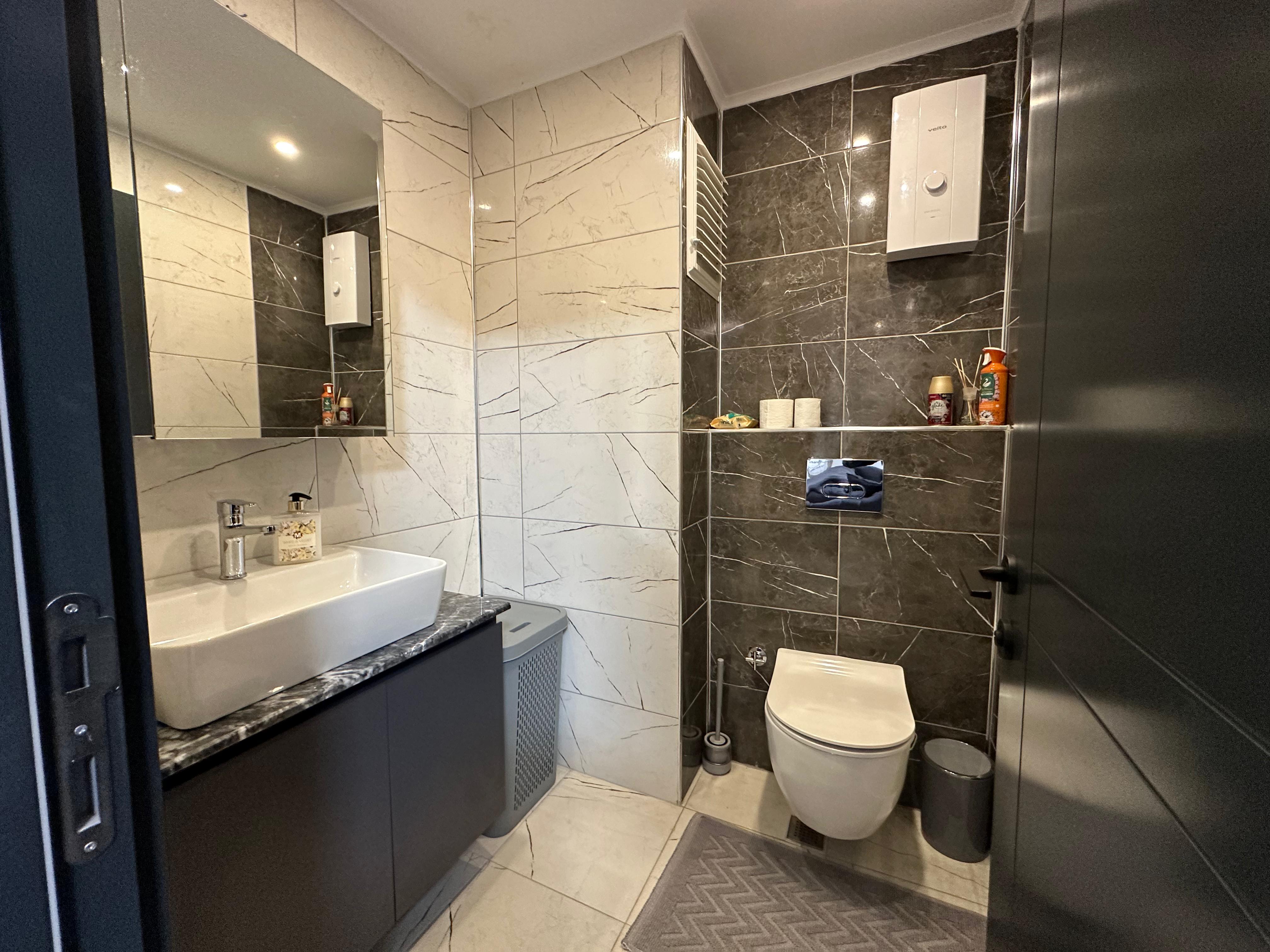 Bathroom with a vessel sink, illuminated mirror and marble-patterned tiles in a duplex