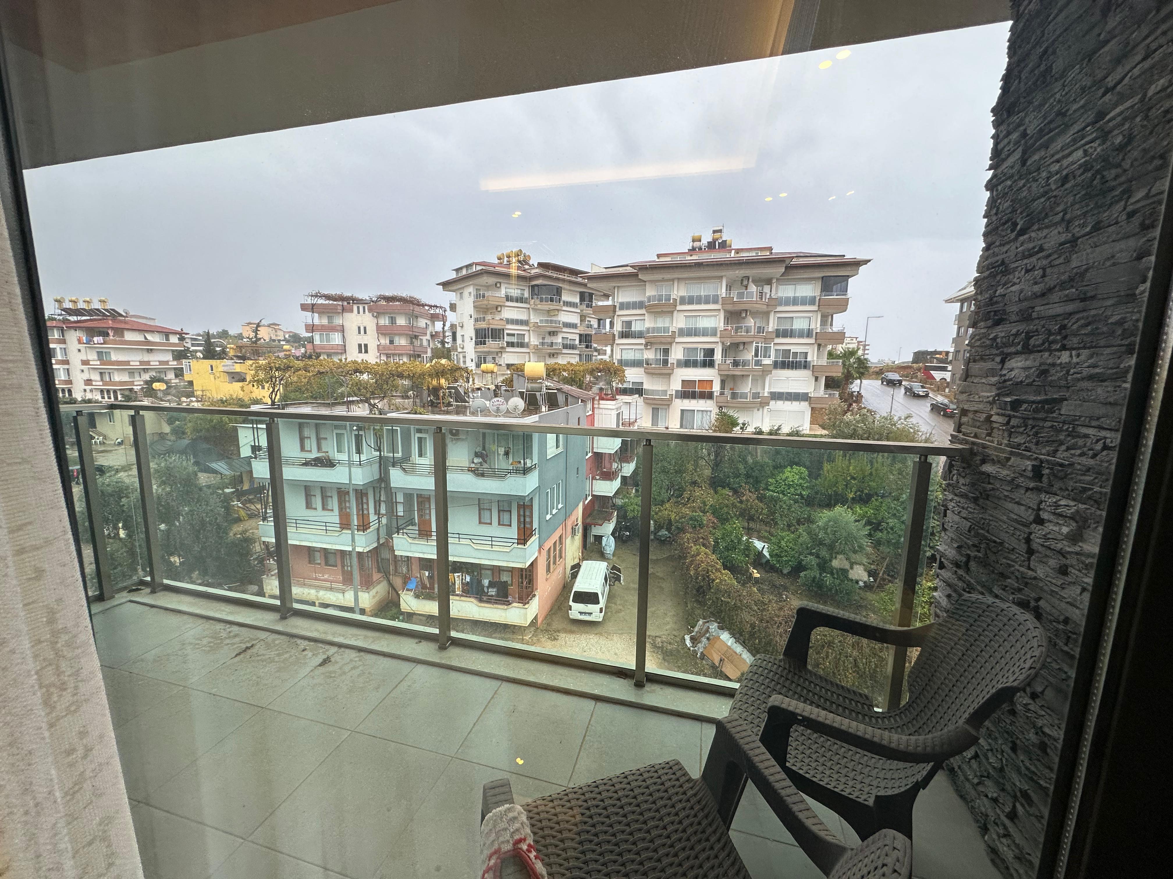 Glazed terrace with woven chairs, glass railing and stone accent wall at a penthouse