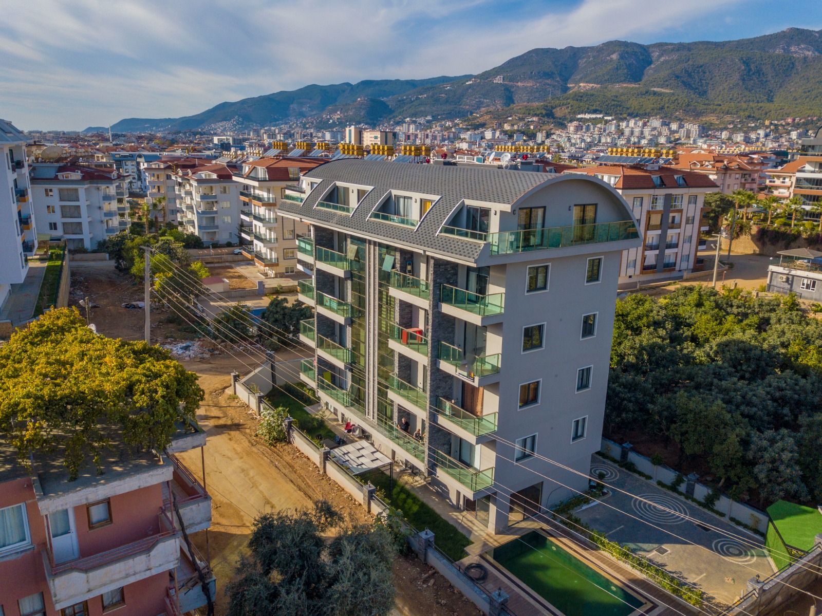 Curved-roof residential tower with glass balconies and mountain backdrop, top-floor apartment in Turkey for sale