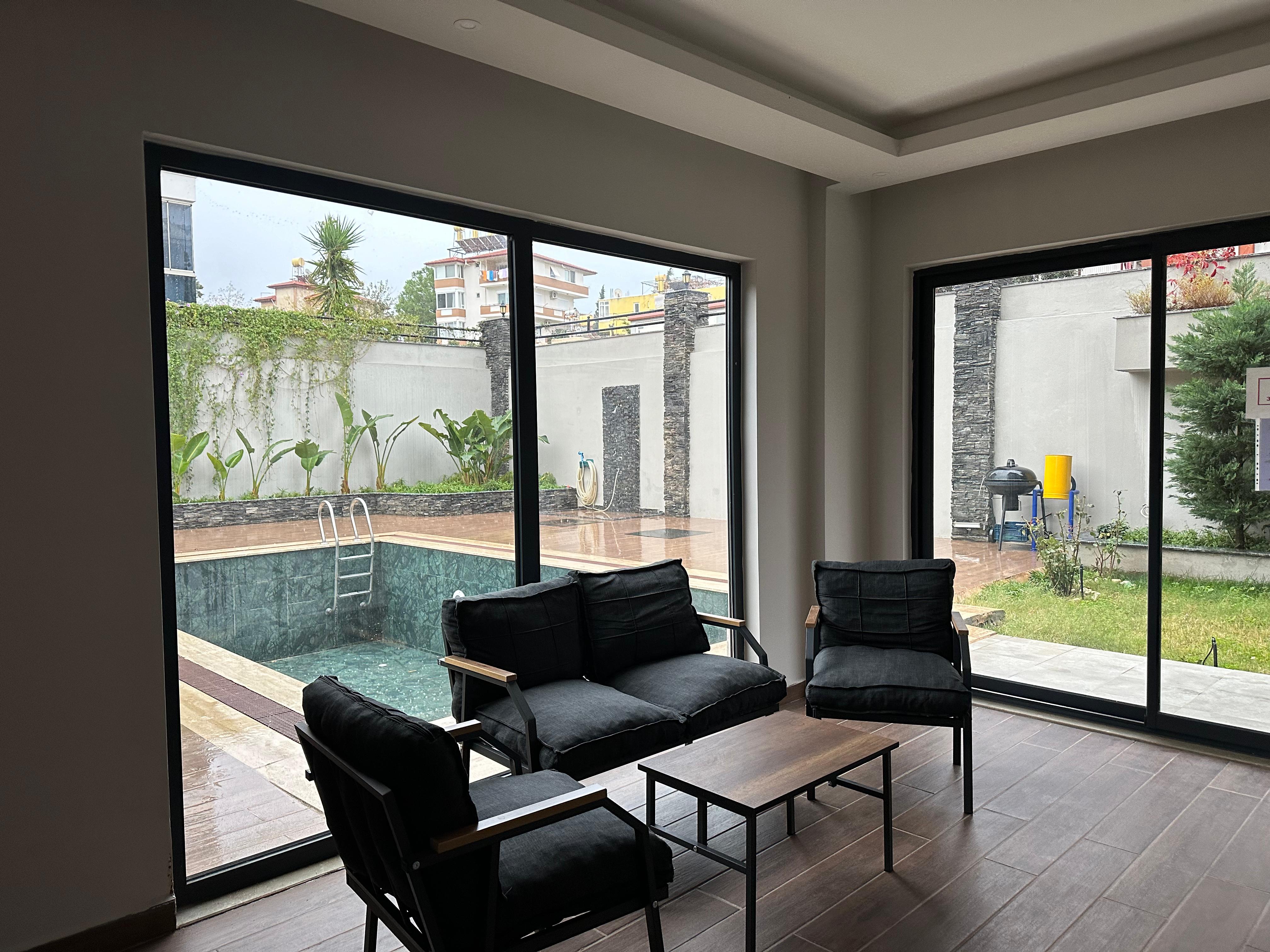 Living room with black sofas and panoramic glazing overlooking a small pool in a residence for sale in Turkey