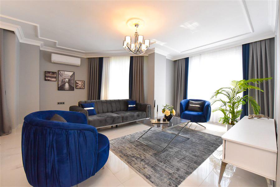 Gri kanepeli ve mavi berjerli salon Oba’da satılık penthouse içinde panoramik pencereye bakıyor