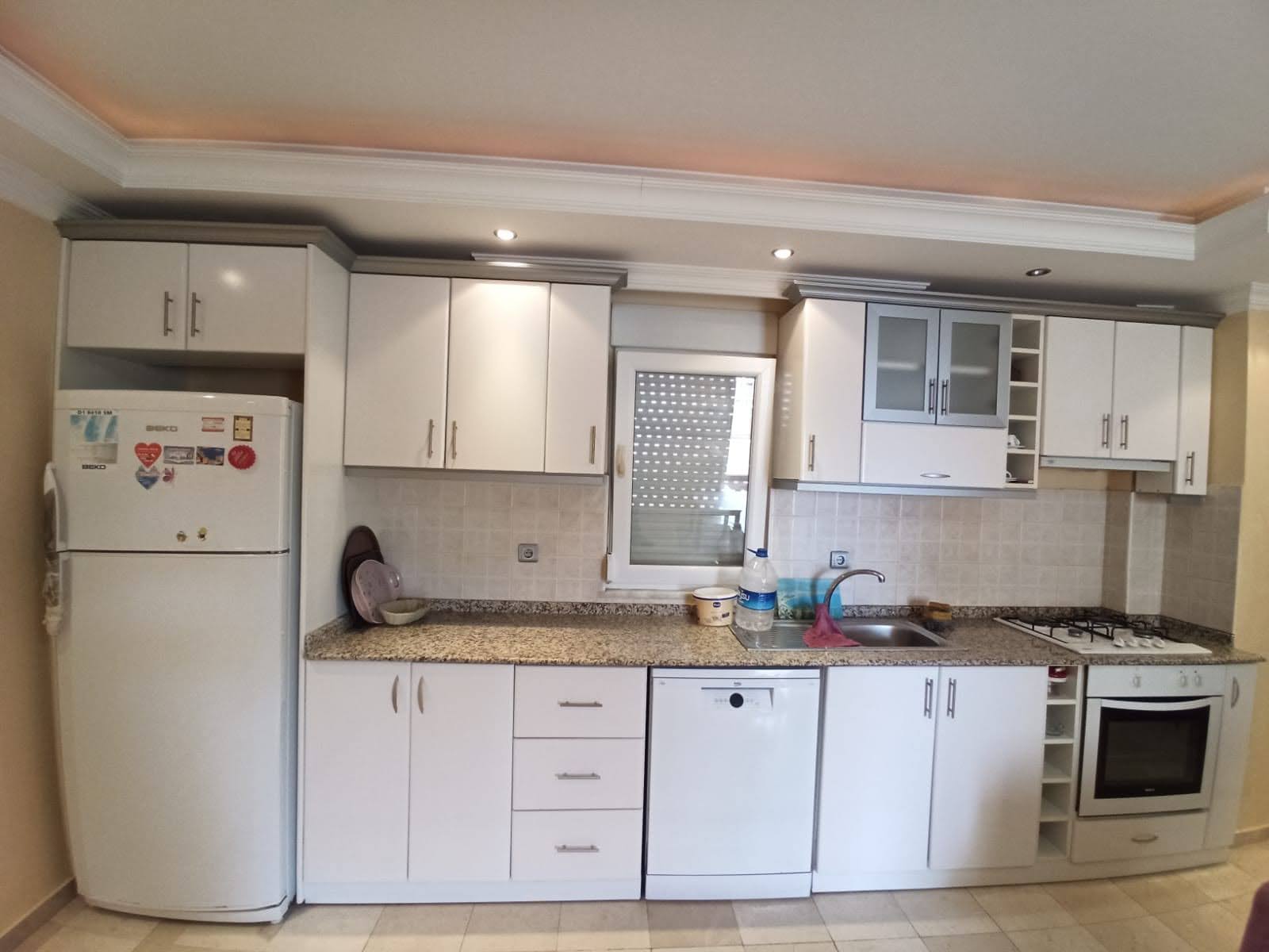 Apartman dairesinin mutfağında beyaz dolaplar, granit tezgâh ve ankastre fırın
