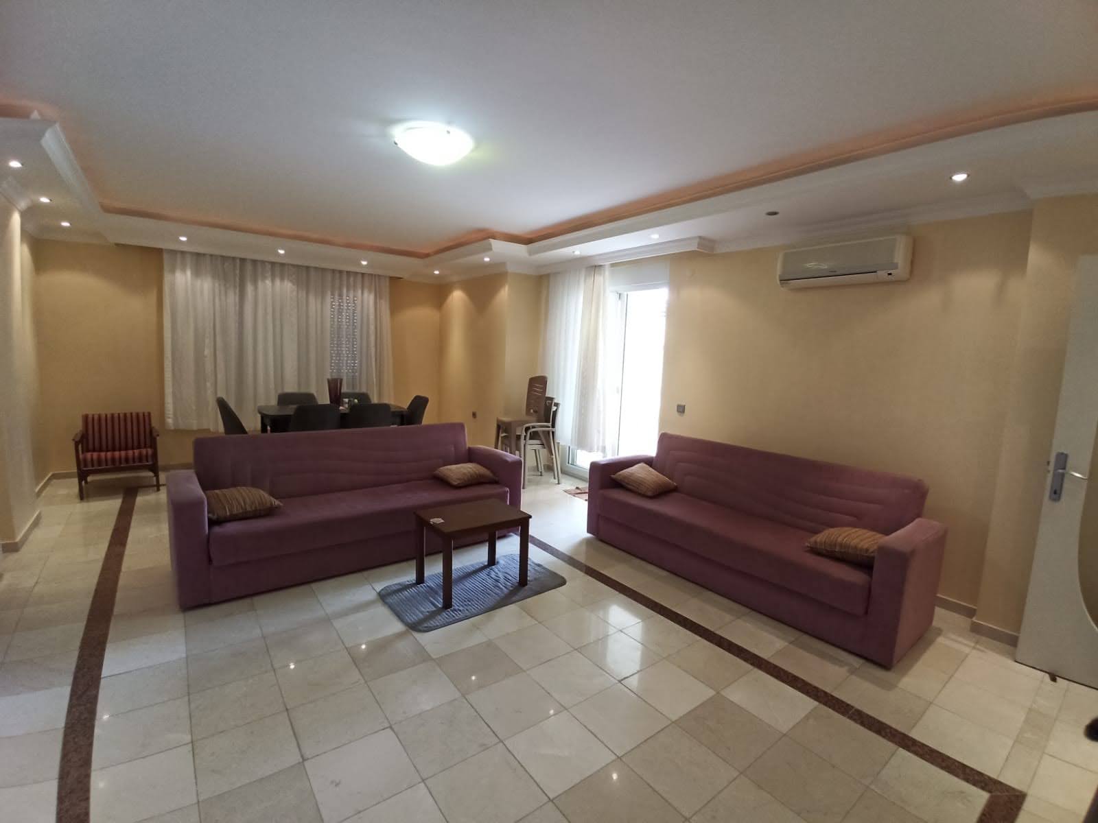 Konutun mutfaklı salonunda iki mor kanepe ve ahşap sehpa
