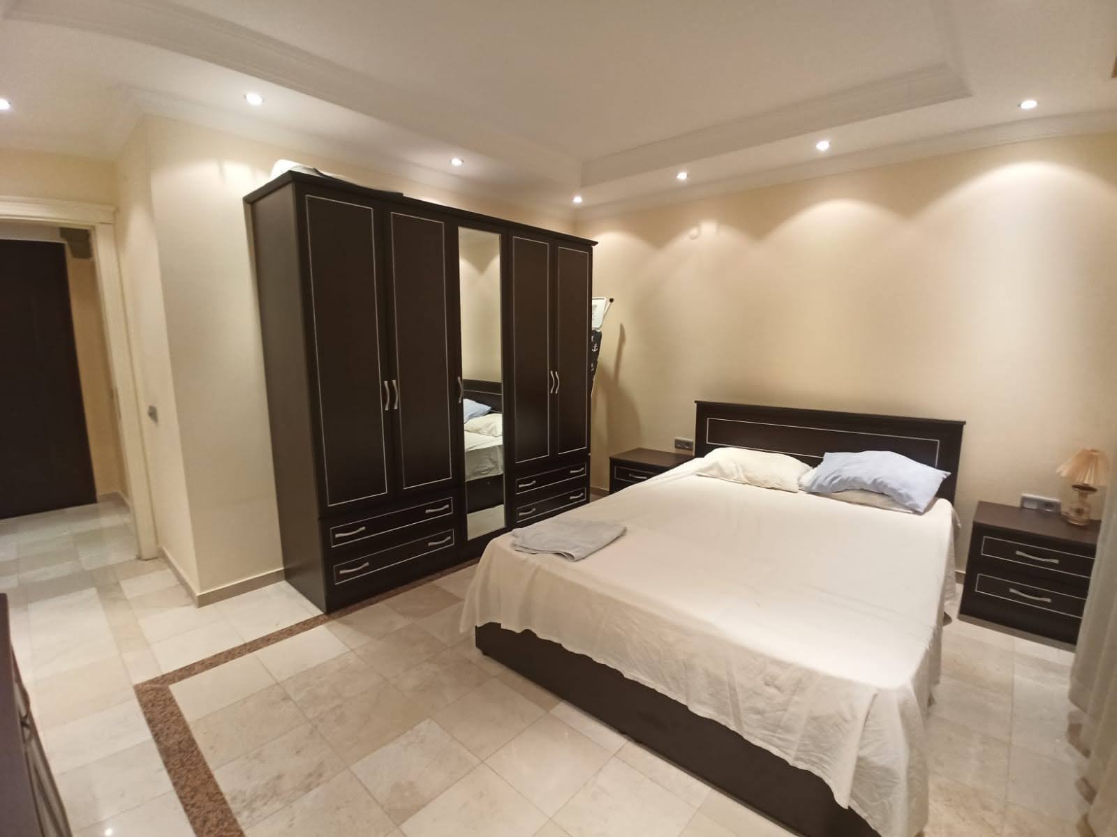 Apartman dairesinin yatak odasında beyaz örtülü yatak ve aynalı kapaklı dolap