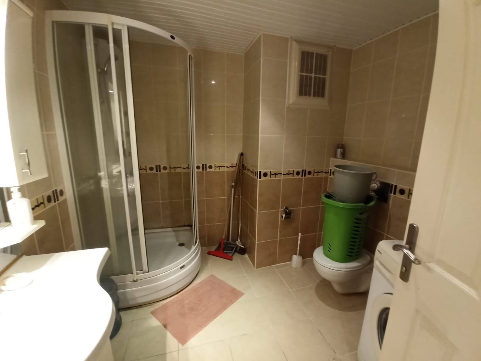Banyoda köşe duş kabini, çamaşır makinesi ve bej duvar karoları