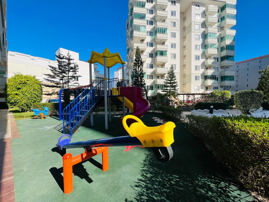 Sarı çatılı oyun kompleksi, mor helezon kaydırak ve yeşil kauçuk zeminli çocuk oyun alanı