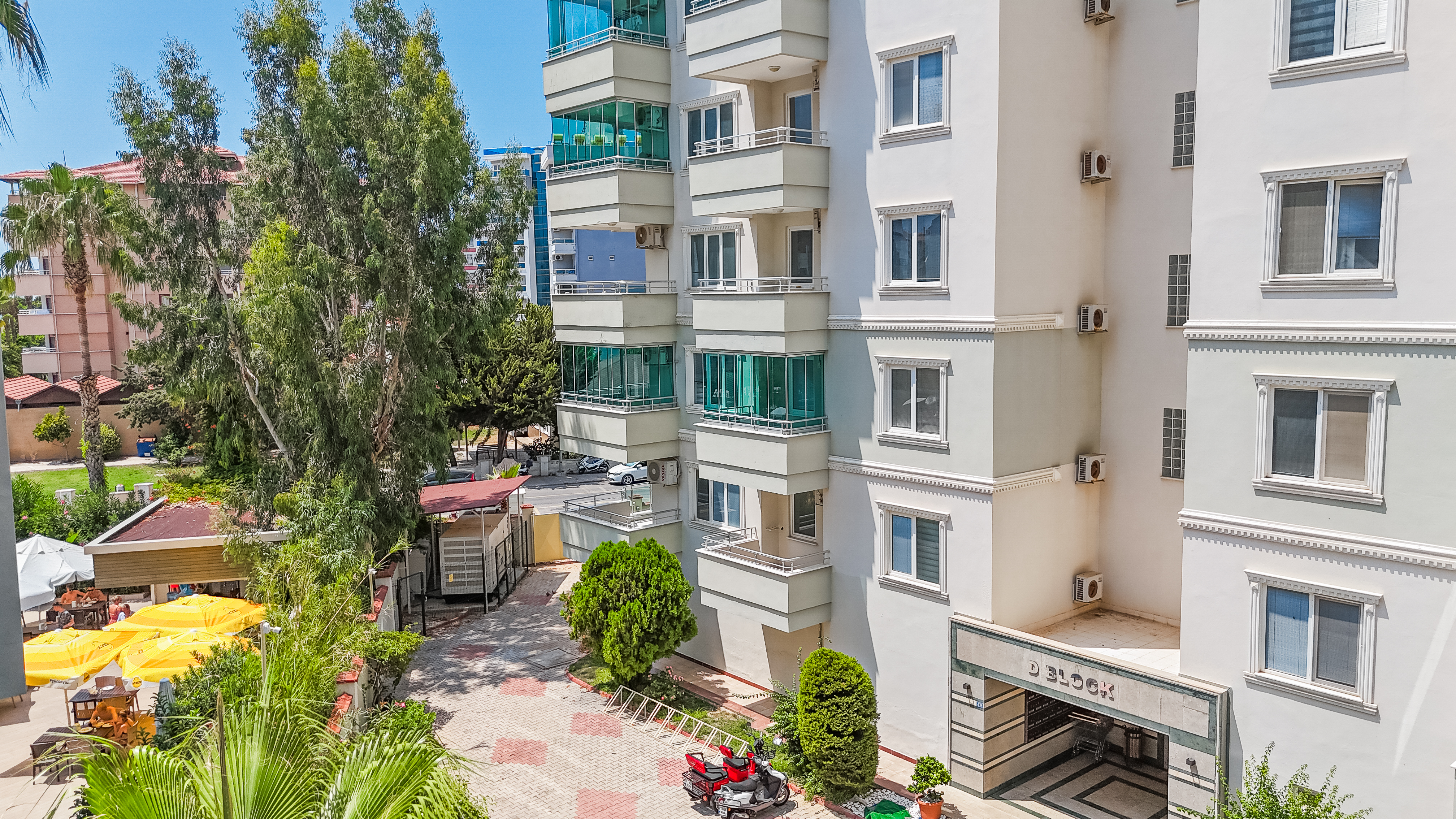 Satılık dairelerin bulunduğu sitede turkuaz cam balkonlu açık renkli bina cephesi