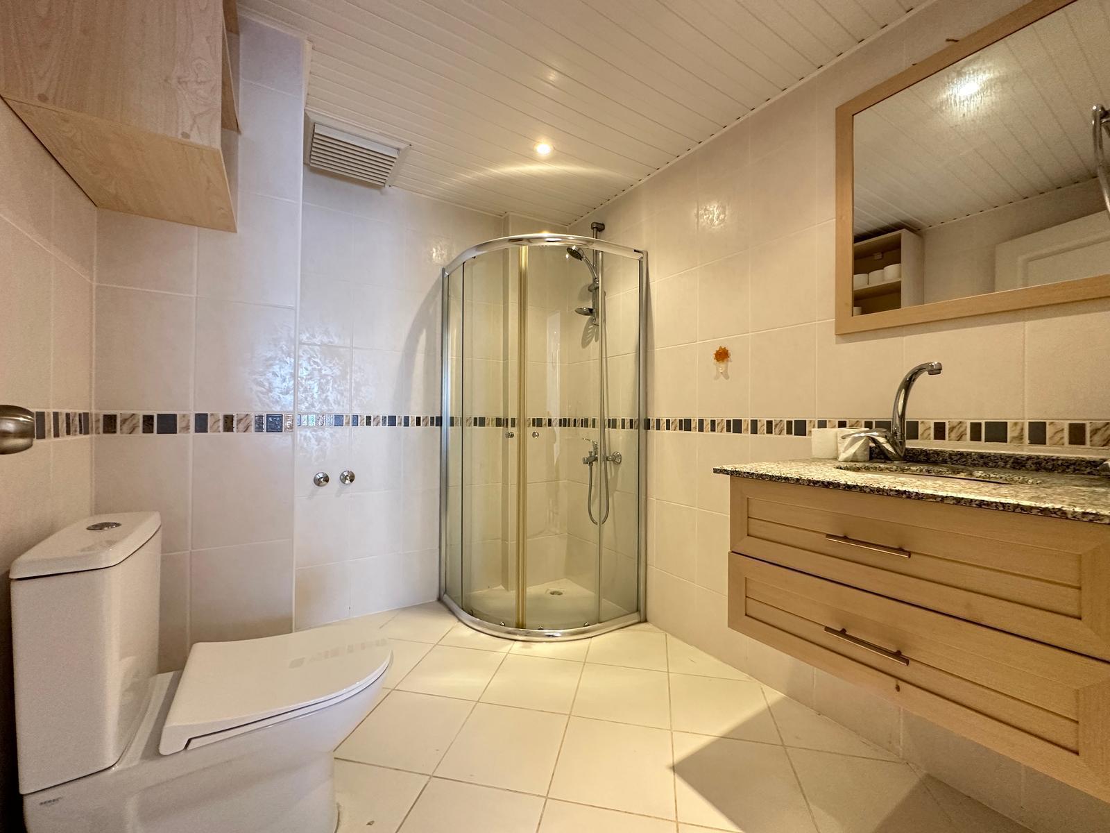 Şeffaf köşe duş kabini, granit tezgâh ve ahşap çerçeveli aynalı banyo, dairede