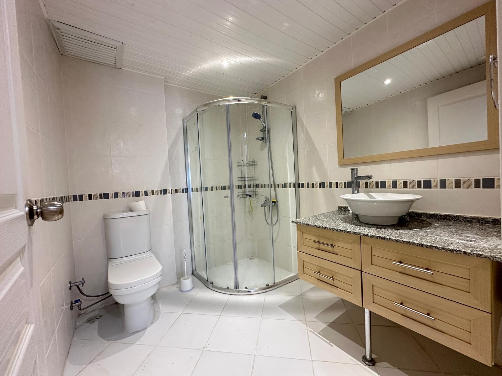 Oval lavabo, cam köşe duş kabini ve geniş ahşap çerçeveli aynalı banyo, Tosmur’da dairede