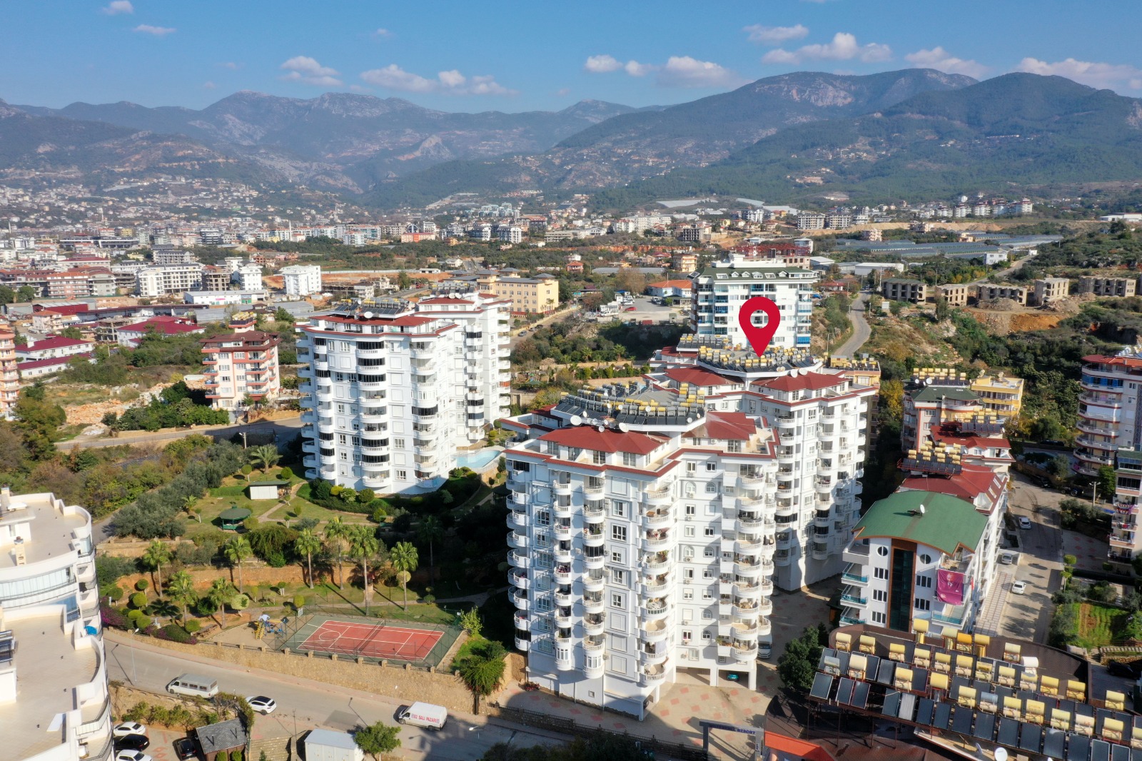 Yuvarlak balkonlu beyaz bloklar ve spor kortu, Tosmur’da Türkiye’de dairelerin bulunduğu sitede