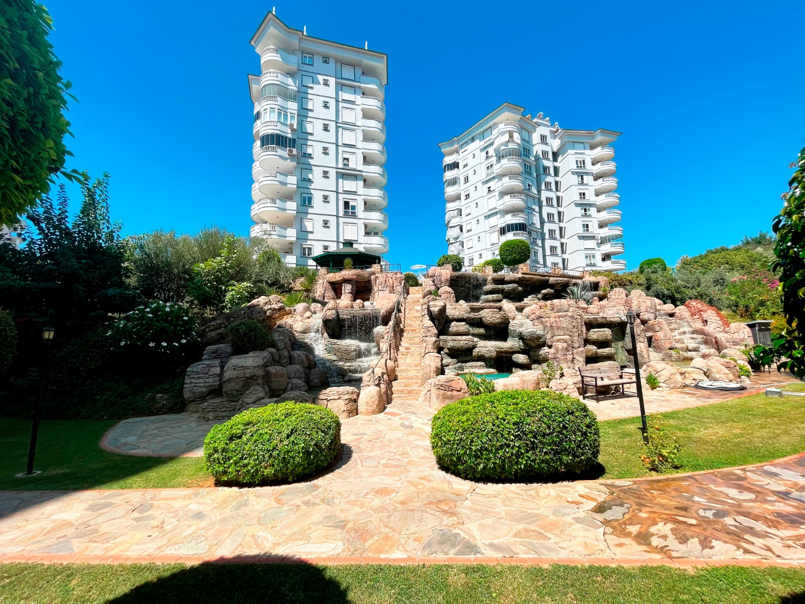 Geniş taş şelale, merkez basamaklar ve yuvarlak budanmış çalıların olduğu iç avlu